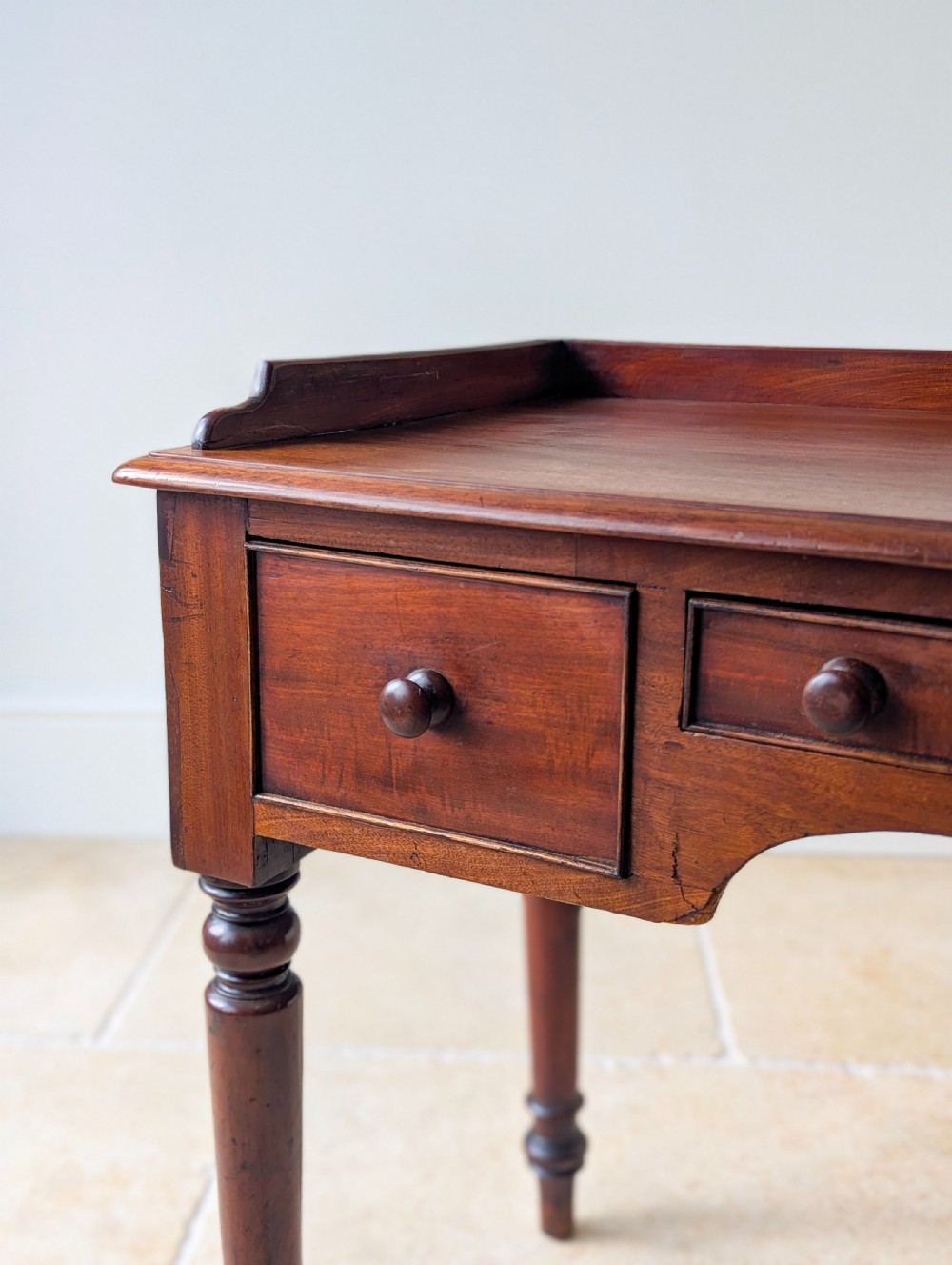 A late Victorian mahogany writing table featuring a low gallery top, three frieze drawers with turned wooden knobs, an arched kneehole, and four turned legs. View V