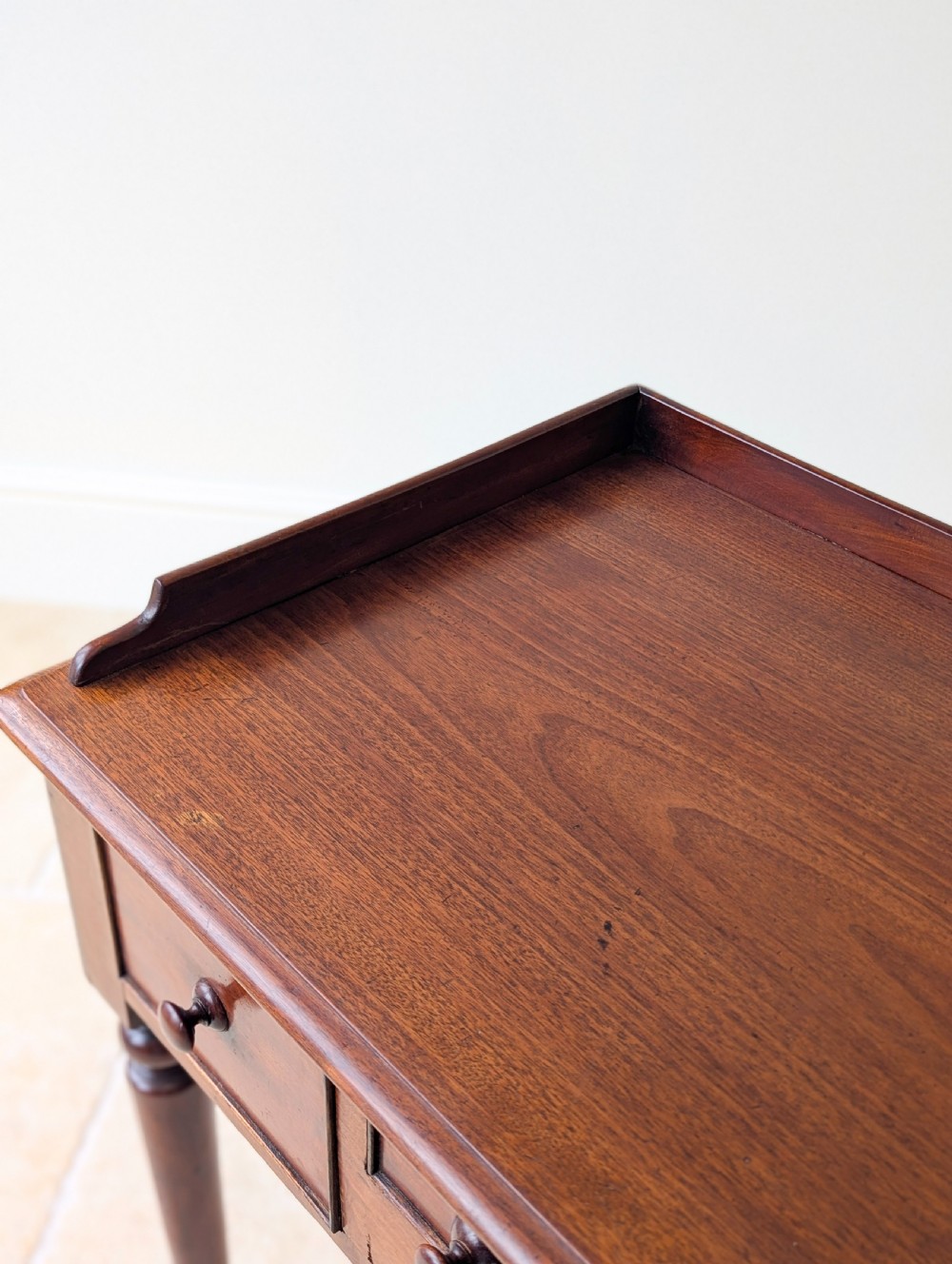 A late Victorian mahogany writing table featuring a low gallery top, three frieze drawers with turned wooden knobs, an arched kneehole, and four turned legs. View VII
