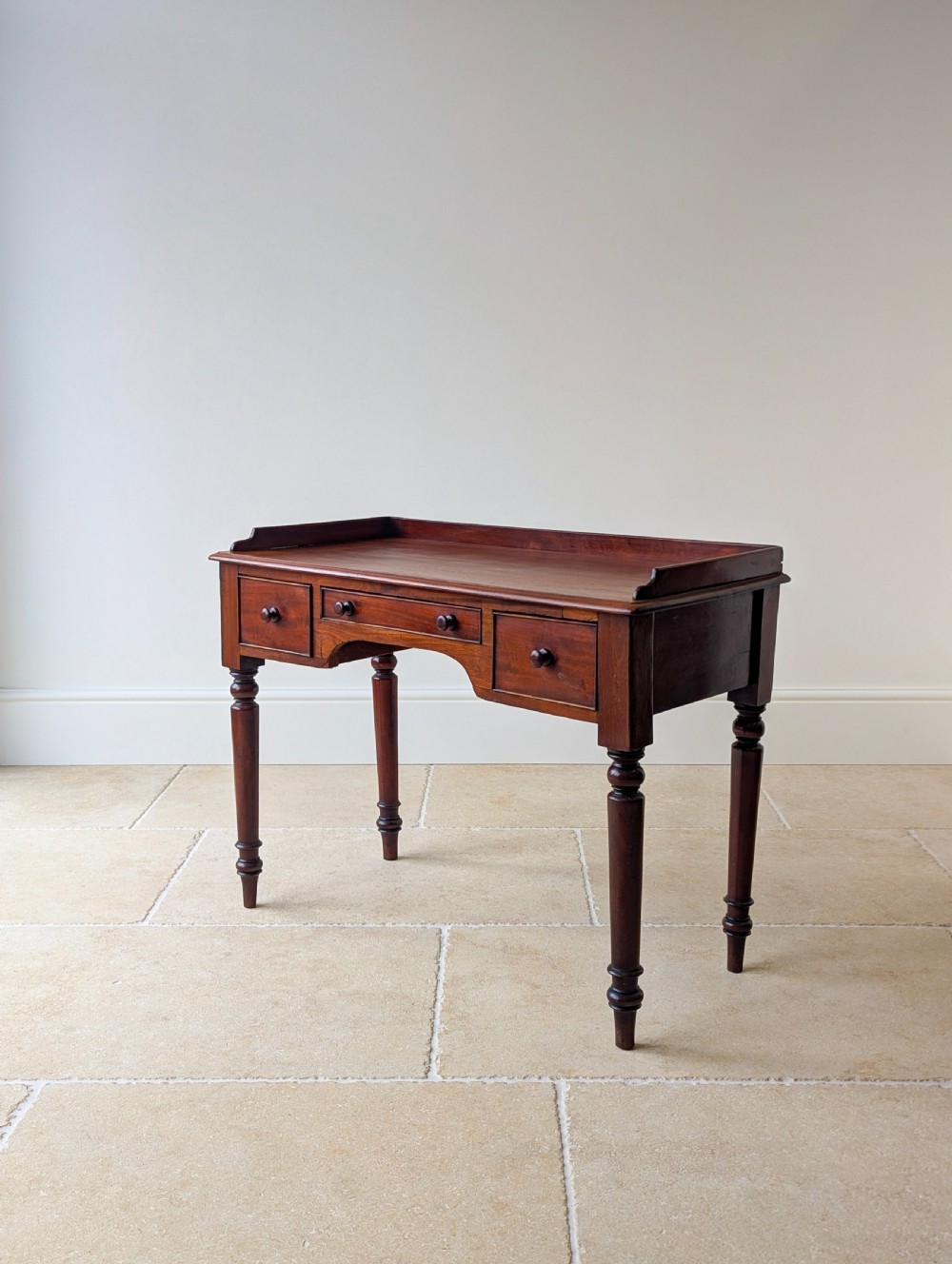 A late Victorian mahogany writing table featuring a low gallery top, three frieze drawers with turned wooden knobs, an arched kneehole, and four turned legs. View VIII