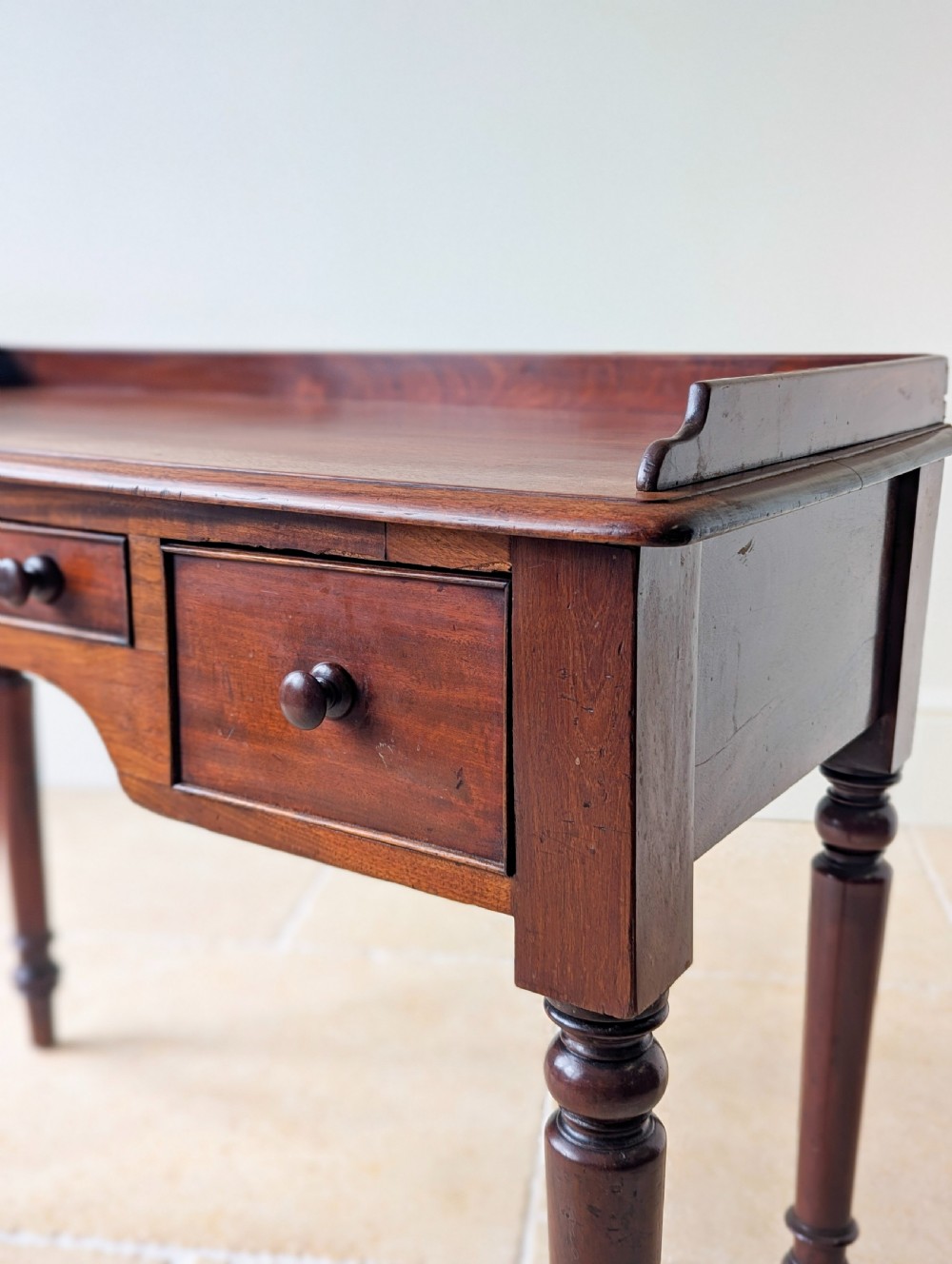 A late Victorian mahogany writing table featuring a low gallery top, three frieze drawers with turned wooden knobs, an arched kneehole, and four turned legs. View IX