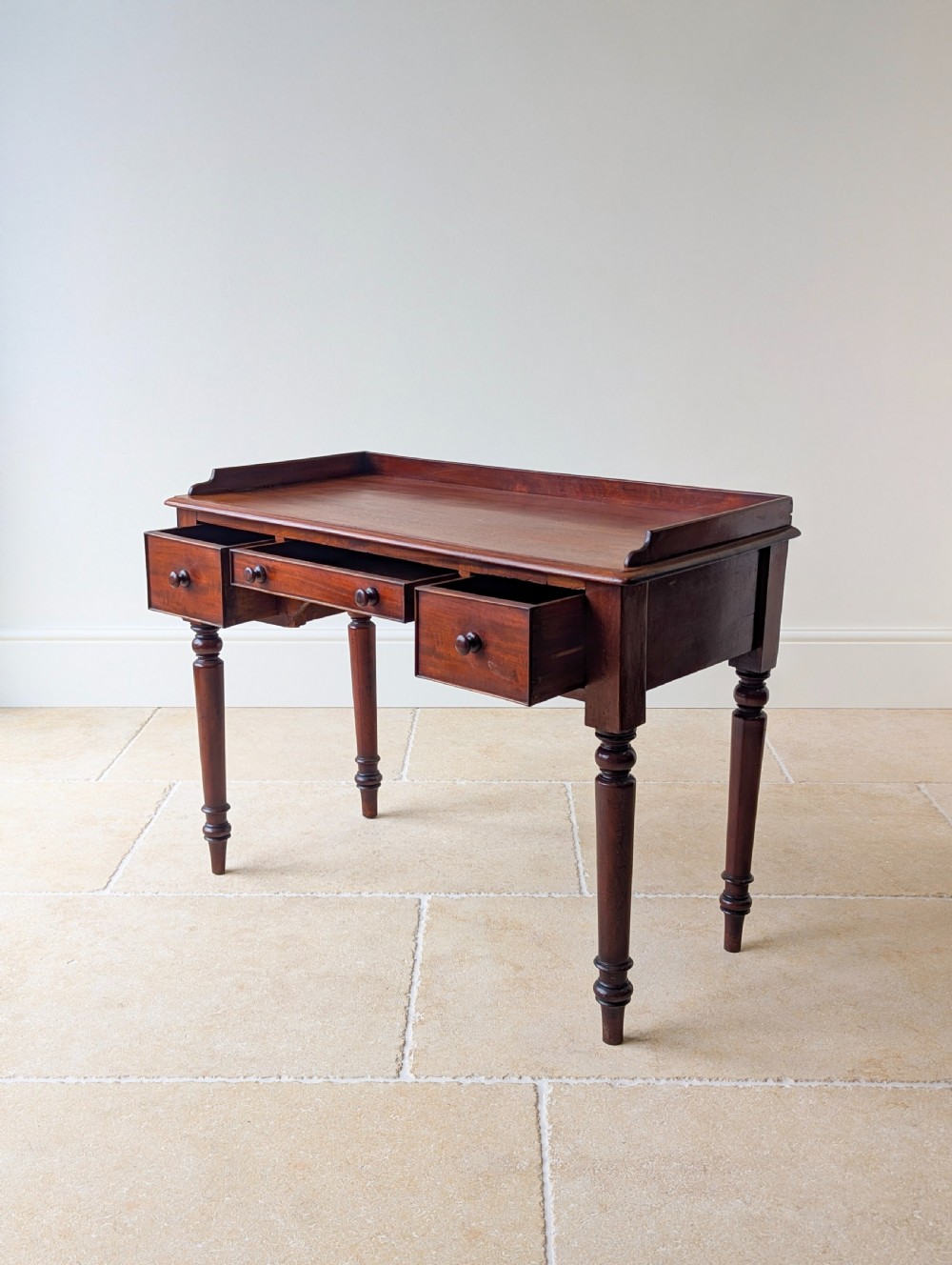 A late Victorian mahogany writing table featuring a low gallery top, three frieze drawers with turned wooden knobs, an arched kneehole, and four turned legs. View X