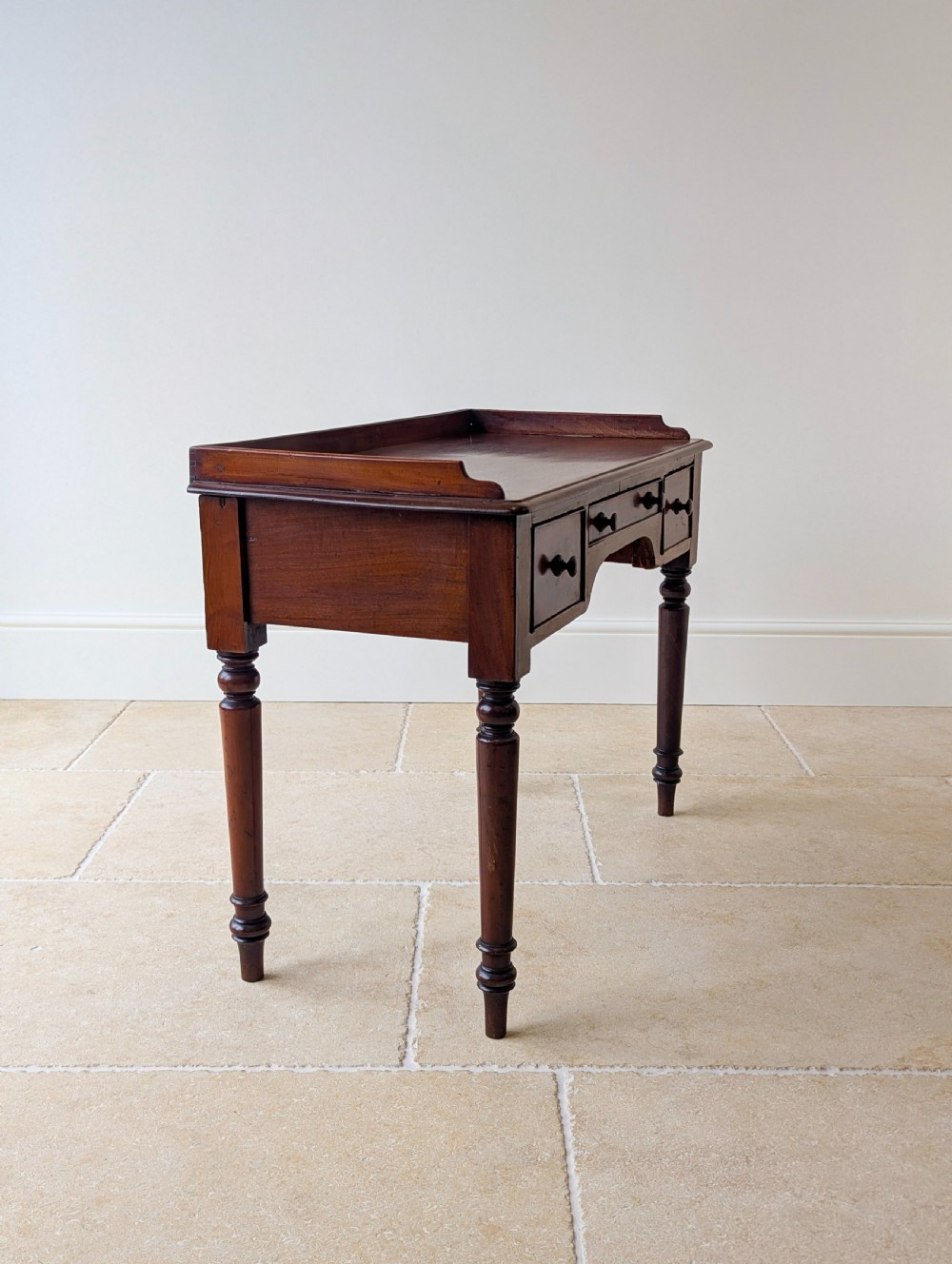 A late Victorian mahogany writing table featuring a low gallery top, three frieze drawers with turned wooden knobs, an arched kneehole, and four turned legs. View XI
