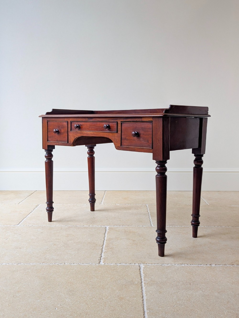 A late Victorian mahogany writing table featuring a low gallery top, three frieze drawers with turned wooden knobs, an arched kneehole, and four turned legs. View XII