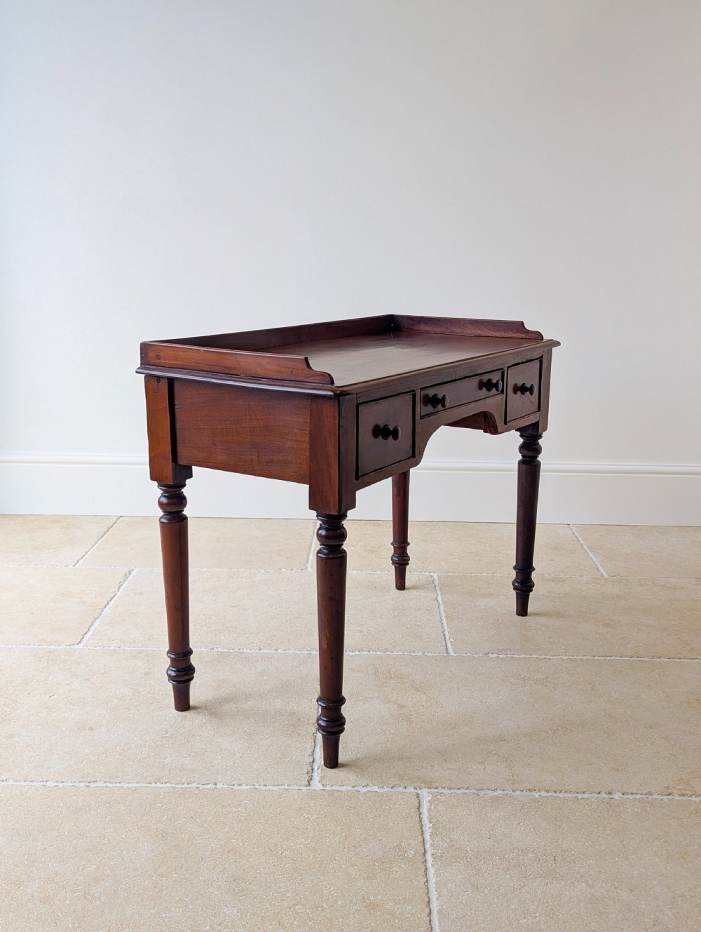 A late Victorian mahogany writing table featuring a low gallery top, three frieze drawers with turned wooden knobs, an arched kneehole, and four turned legs. View XIII