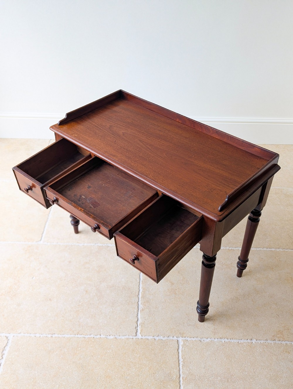 A late Victorian mahogany writing table featuring a low gallery top, three frieze drawers with turned wooden knobs, an arched kneehole, and four turned legs. View XIV