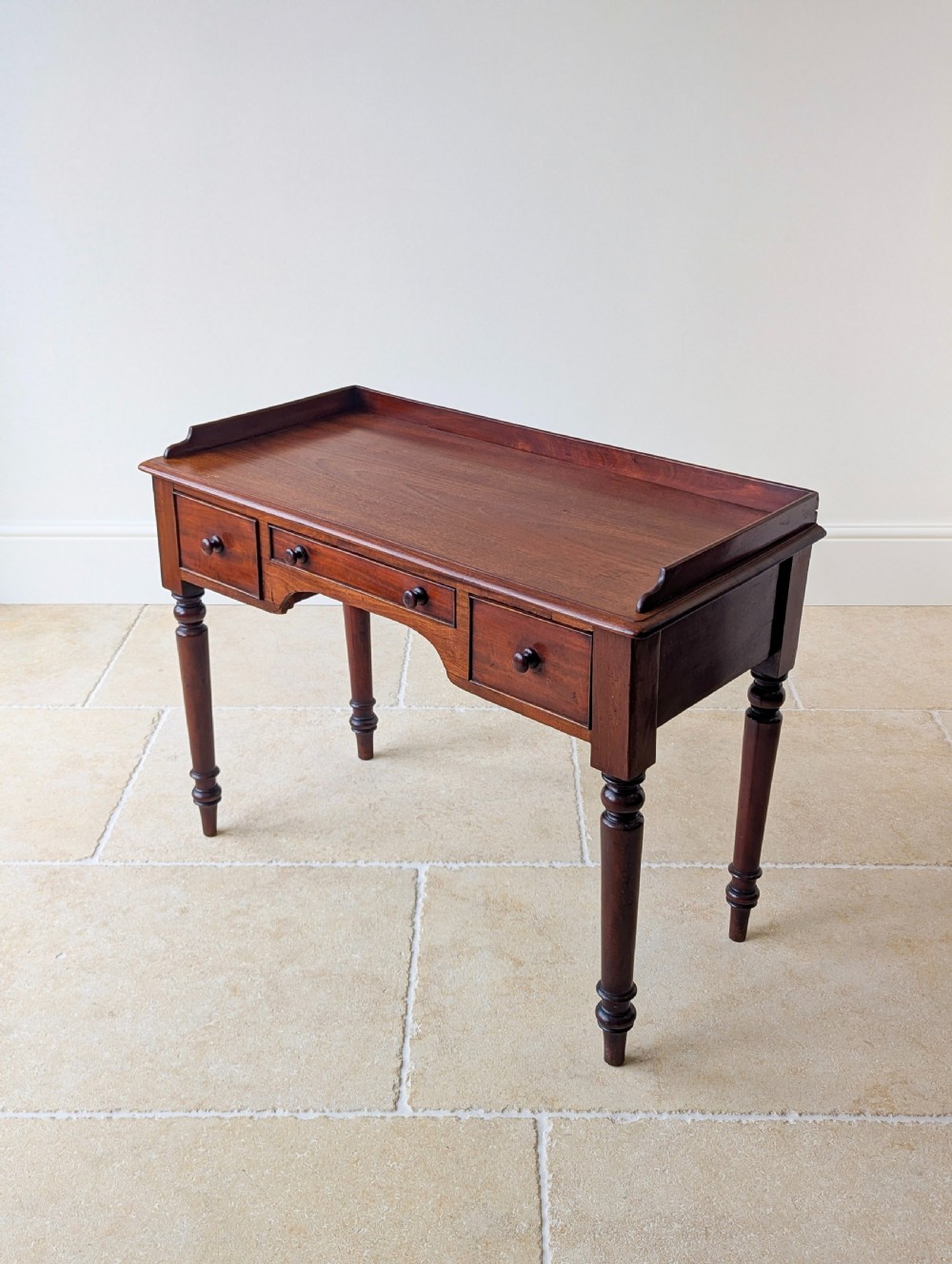 A late Victorian mahogany writing table featuring a low gallery top, three frieze drawers with turned wooden knobs, an arched kneehole, and four turned legs. View XV