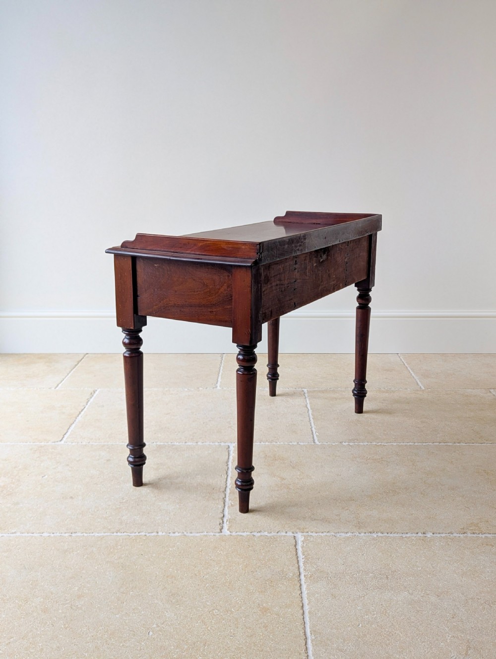 A late Victorian mahogany writing table featuring a low gallery top, three frieze drawers with turned wooden knobs, an arched kneehole, and four turned legs. View XVI