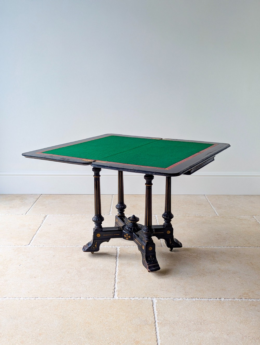 An antique Victorian ebonised and gilt card table with turned twin pedestals and a central finial stretcher. View II