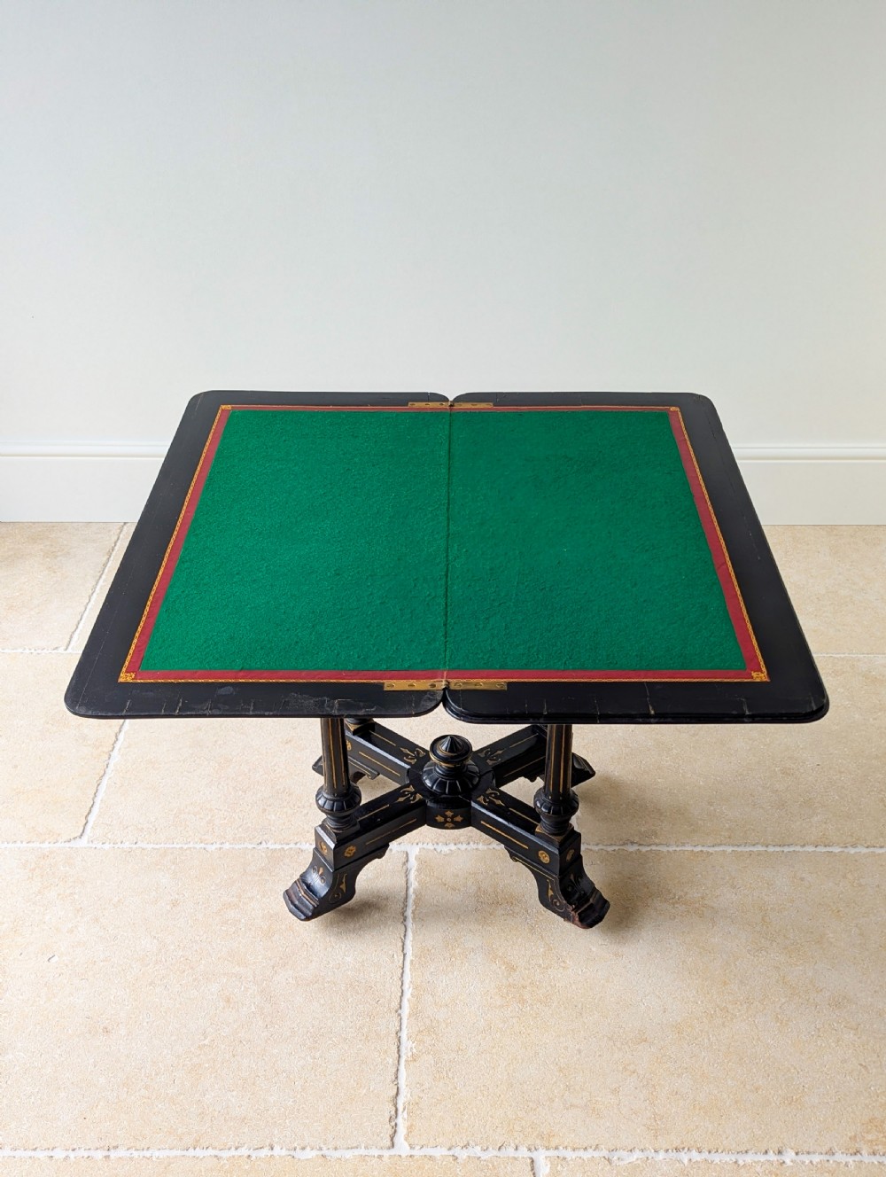 An antique Victorian ebonised and gilt card table with turned twin pedestals and a central finial stretcher. View VI