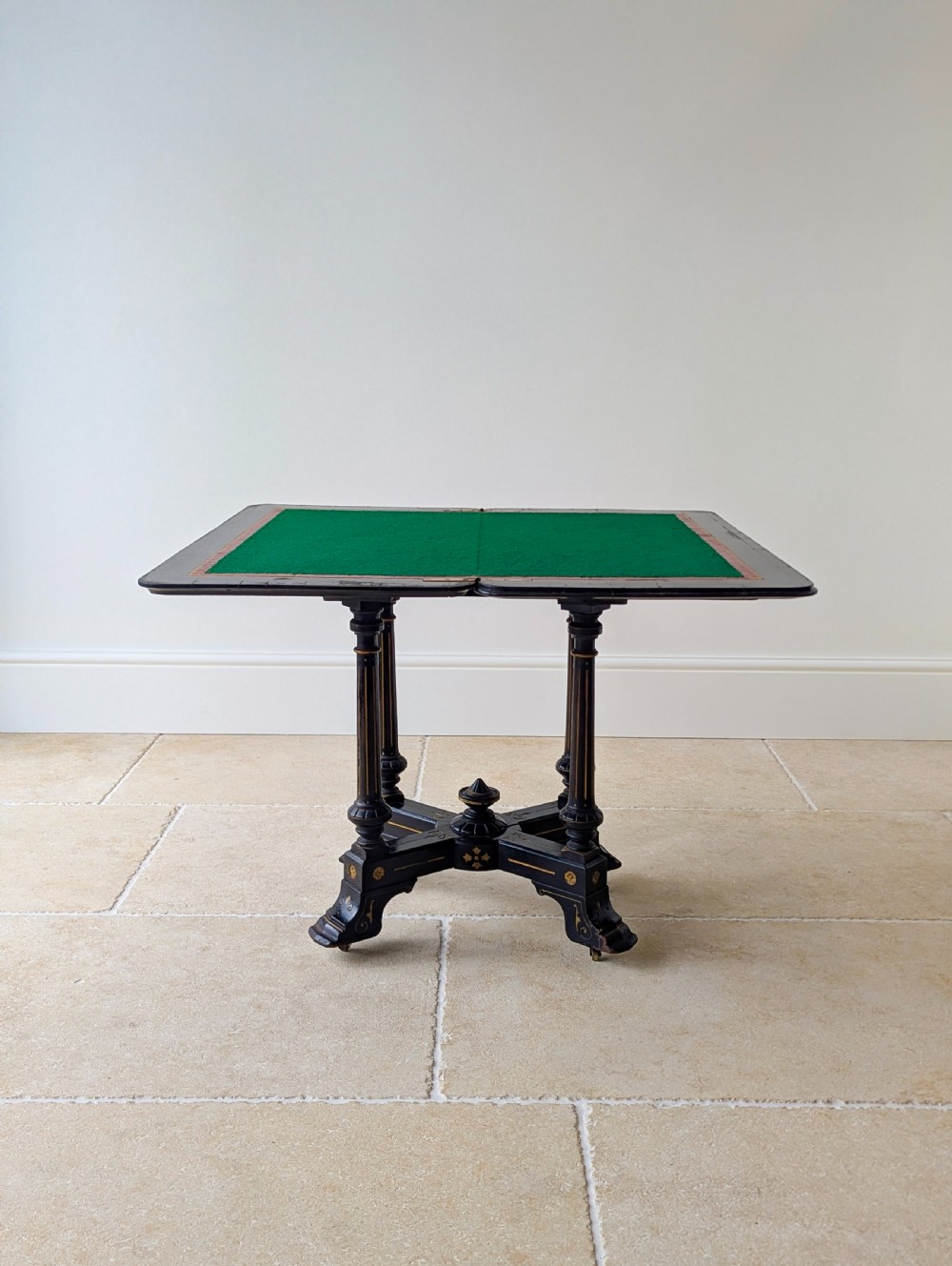 An antique Victorian ebonised and gilt card table with turned twin pedestals and a central finial stretcher. View XV
