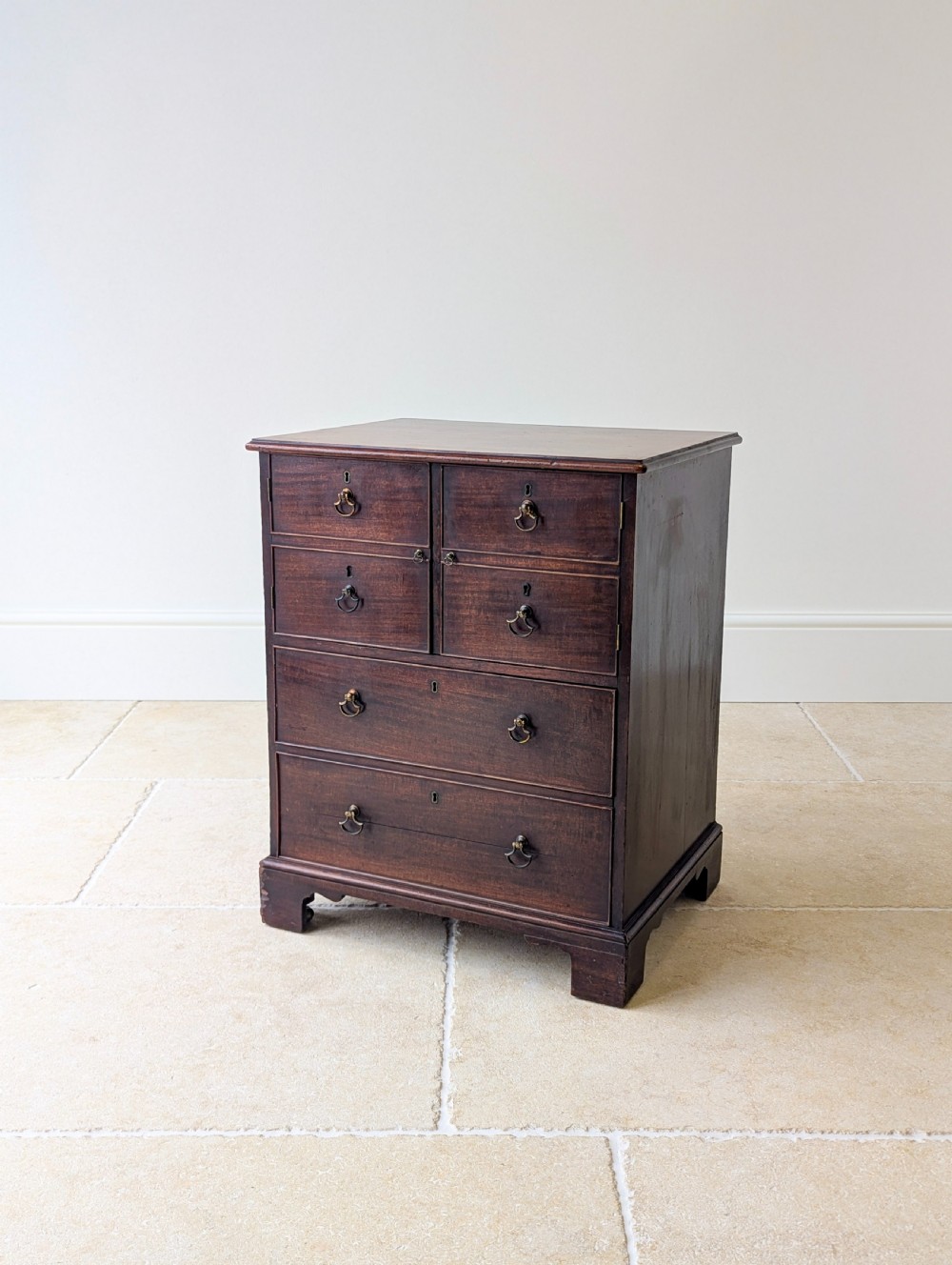 A dark mahogany Georgian commode chest with faux upper drawer fronts, two lower drawers, brass drop handles, and bracket feet.