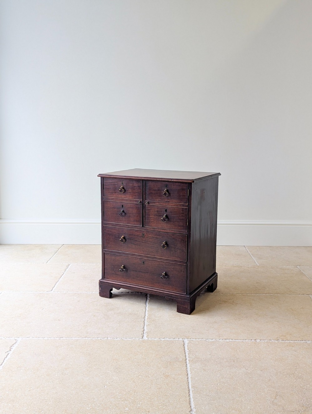 A dark mahogany Georgian commode chest with faux upper drawer fronts, two lower drawers, brass drop handles, and bracket feet. View V