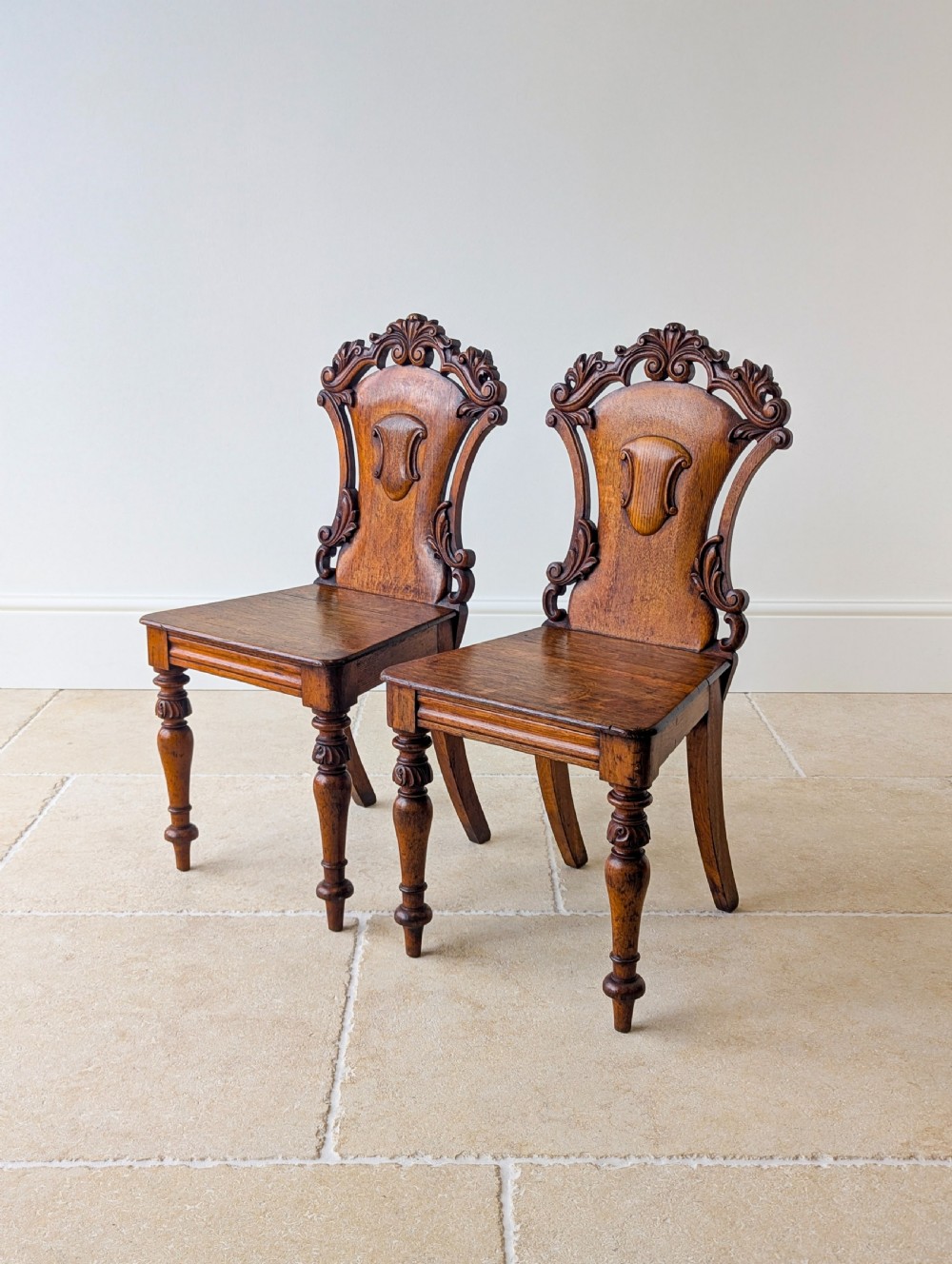 A pair of Victorian oak hall chairs featuring carved cartouche backs, flat wooden seats, and turned front legs. View II