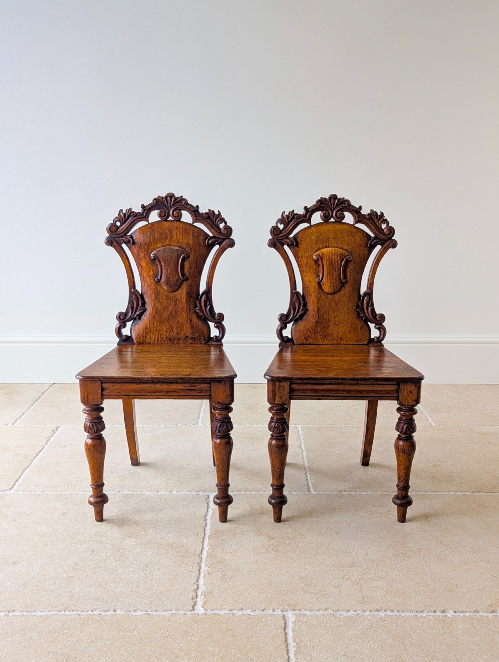 A pair of Victorian oak hall chairs featuring carved cartouche backs, flat wooden seats, and turned front legs. View III