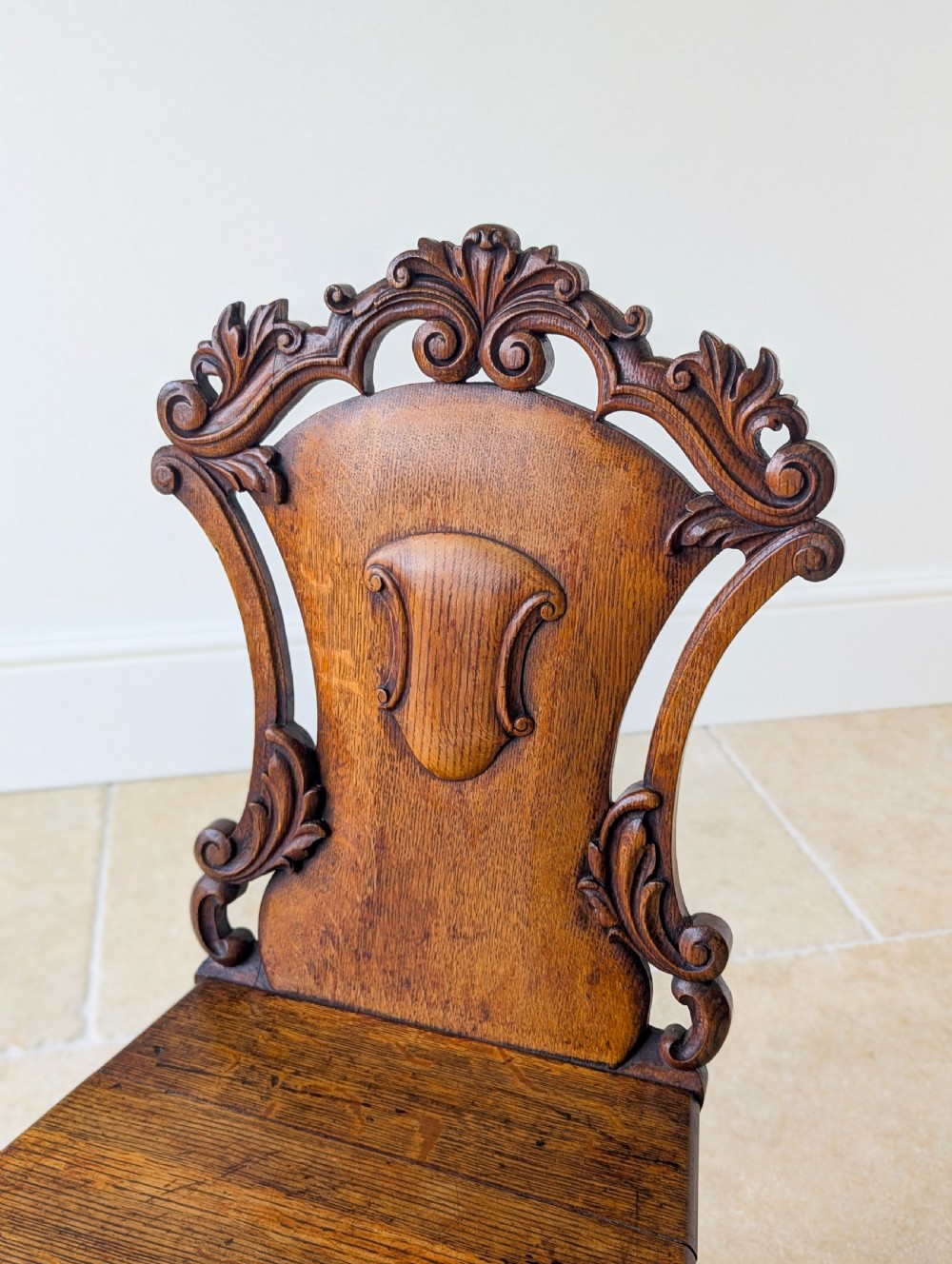 A pair of Victorian oak hall chairs featuring carved cartouche backs, flat wooden seats, and turned front legs. View IV
