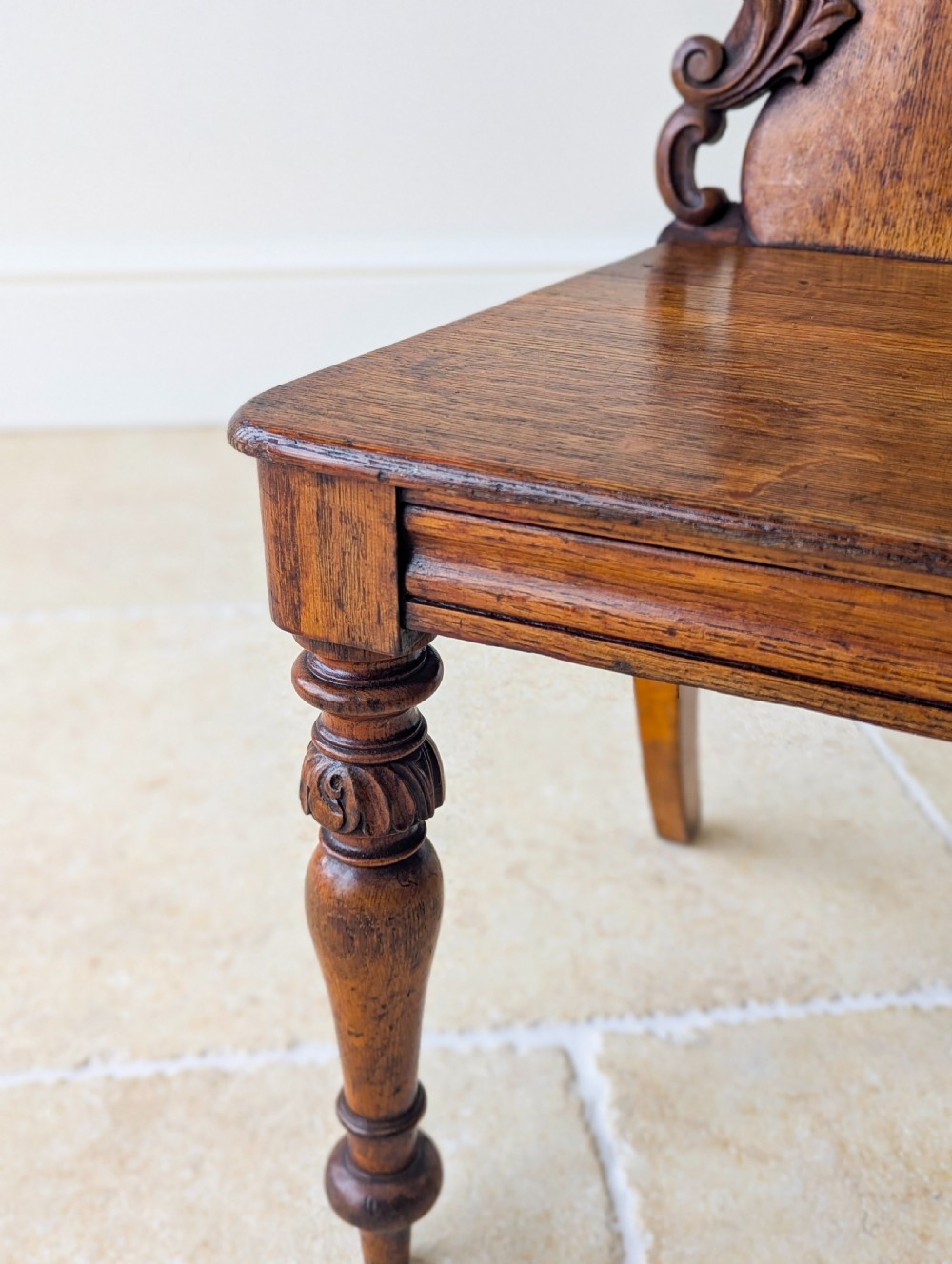 A pair of Victorian oak hall chairs featuring carved cartouche backs, flat wooden seats, and turned front legs. View VI