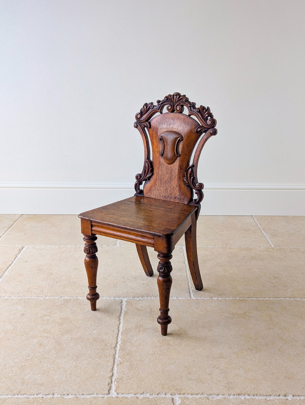 A pair of Victorian oak hall chairs featuring carved cartouche backs, flat wooden seats, and turned front legs. View VIII