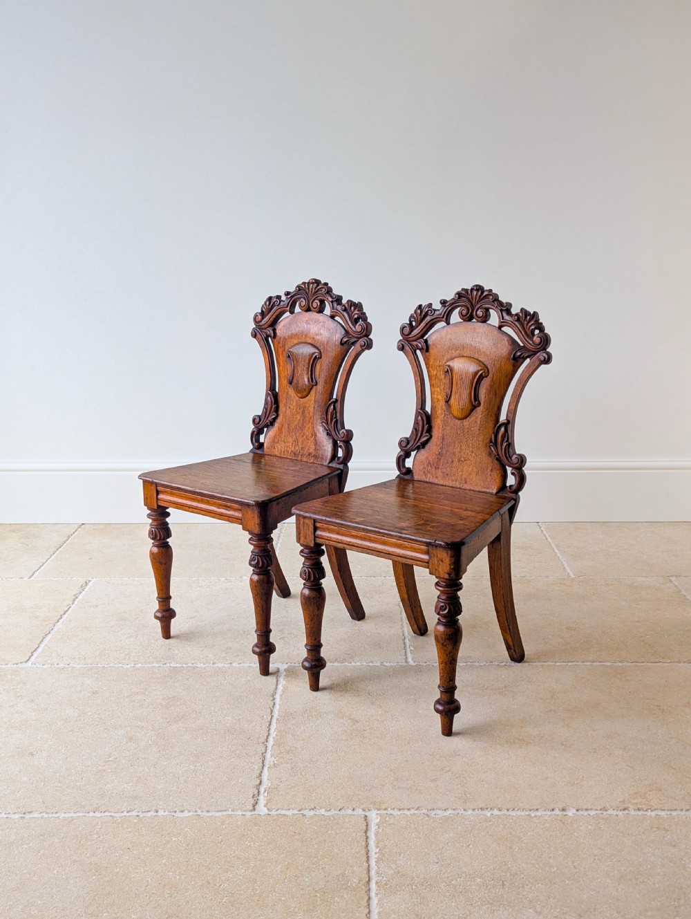 A pair of Victorian oak hall chairs featuring carved cartouche backs, flat wooden seats, and turned front legs. View IX