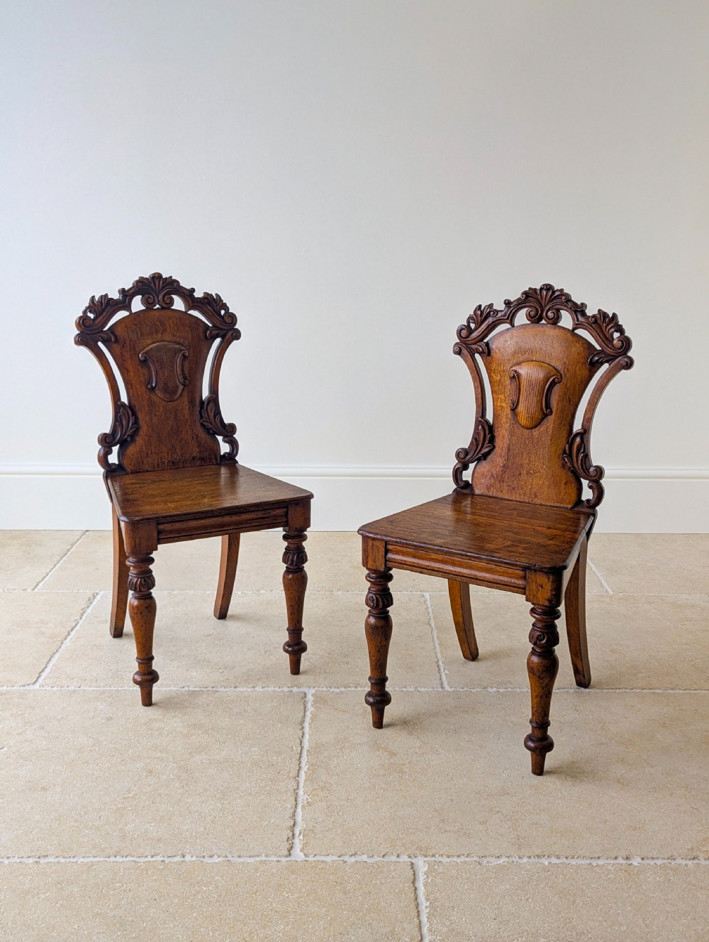 A pair of Victorian oak hall chairs featuring carved cartouche backs, flat wooden seats, and turned front legs. View XI