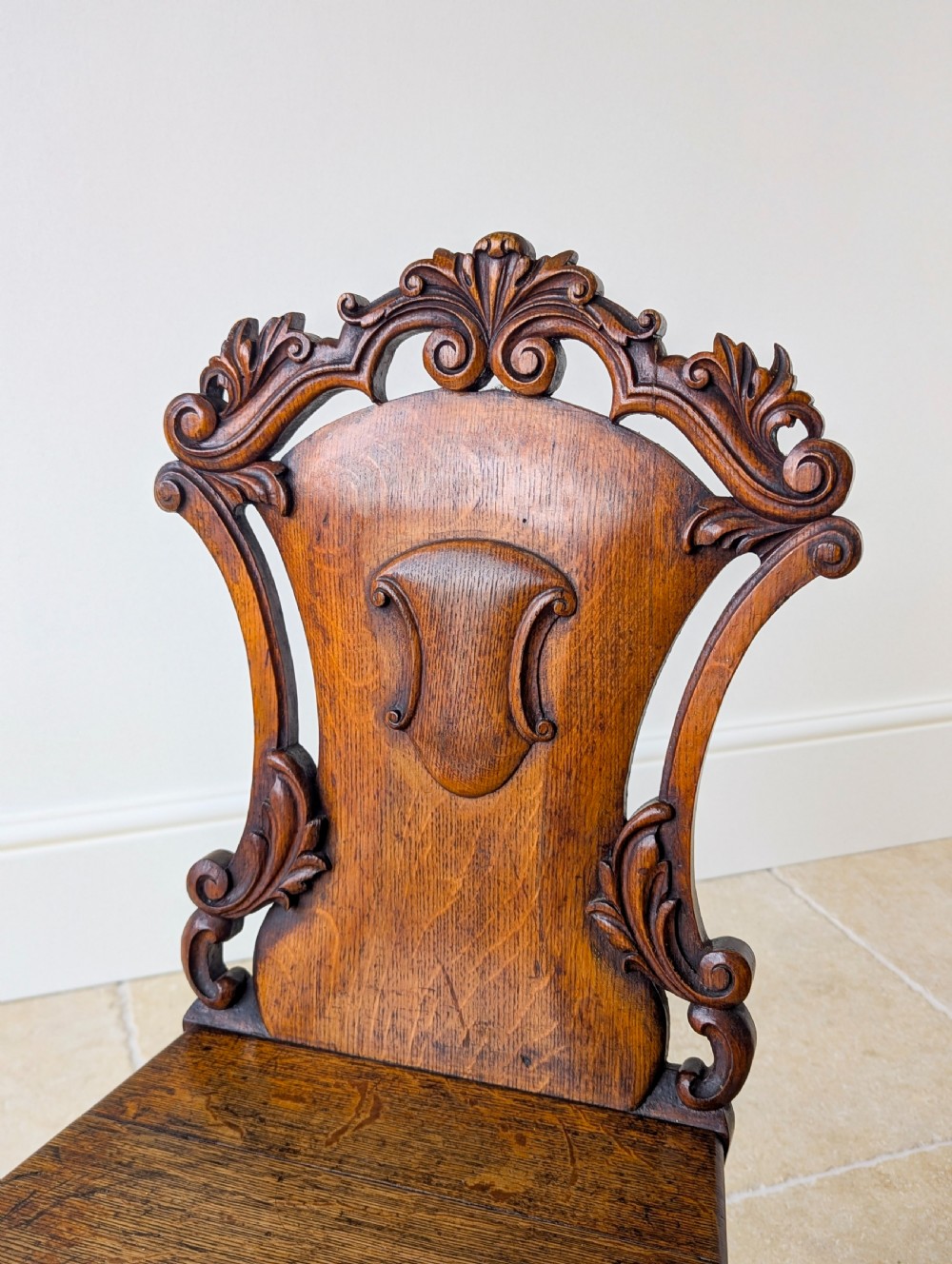 A pair of Victorian oak hall chairs featuring carved cartouche backs, flat wooden seats, and turned front legs. View XII