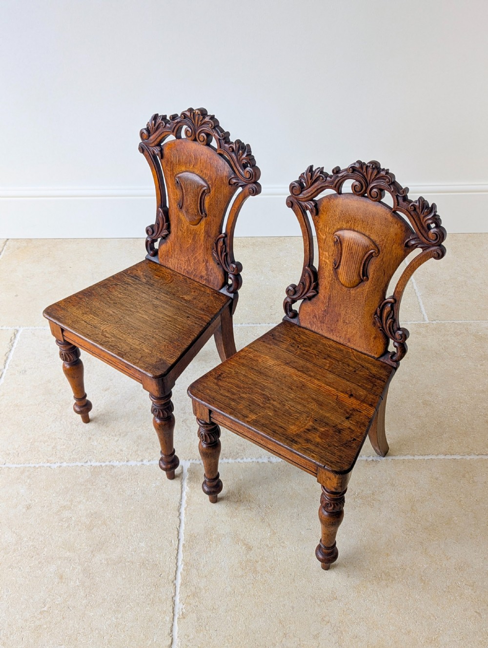 A pair of Victorian oak hall chairs featuring carved cartouche backs, flat wooden seats, and turned front legs. View XIII