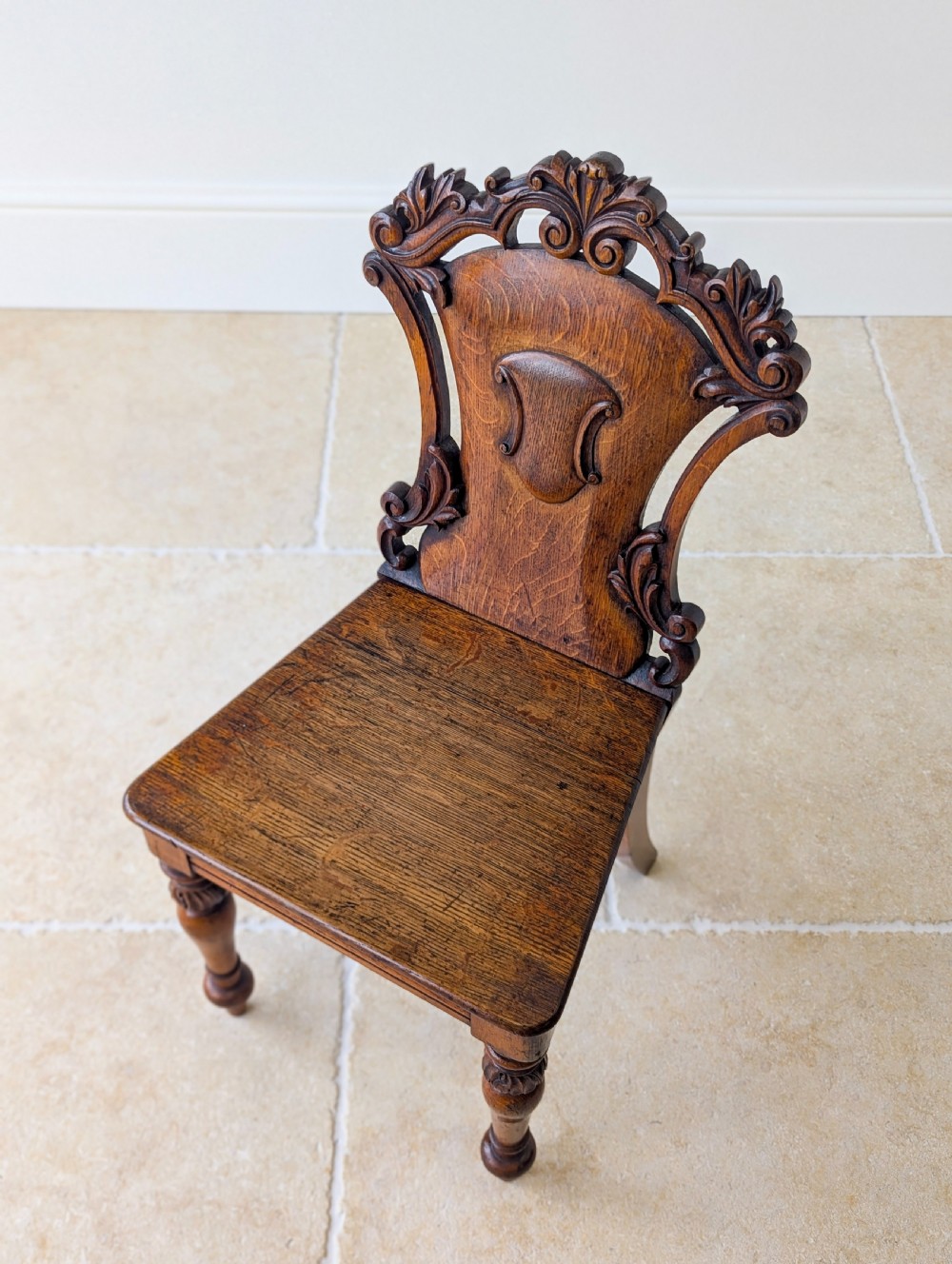 A pair of Victorian oak hall chairs featuring carved cartouche backs, flat wooden seats, and turned front legs. View XIV