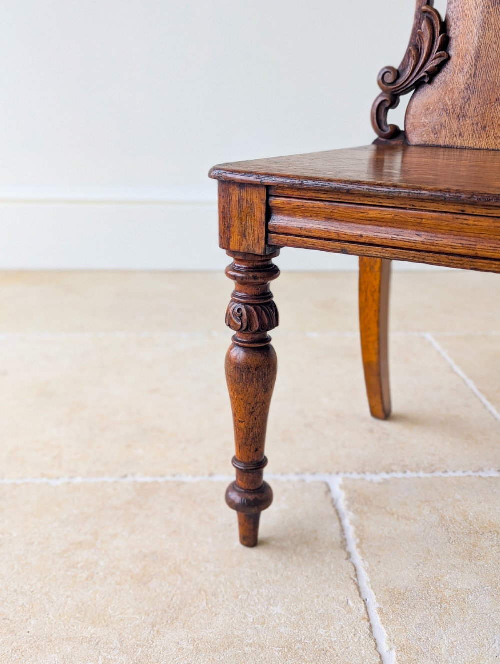 A pair of Victorian oak hall chairs featuring carved cartouche backs, flat wooden seats, and turned front legs. View XV