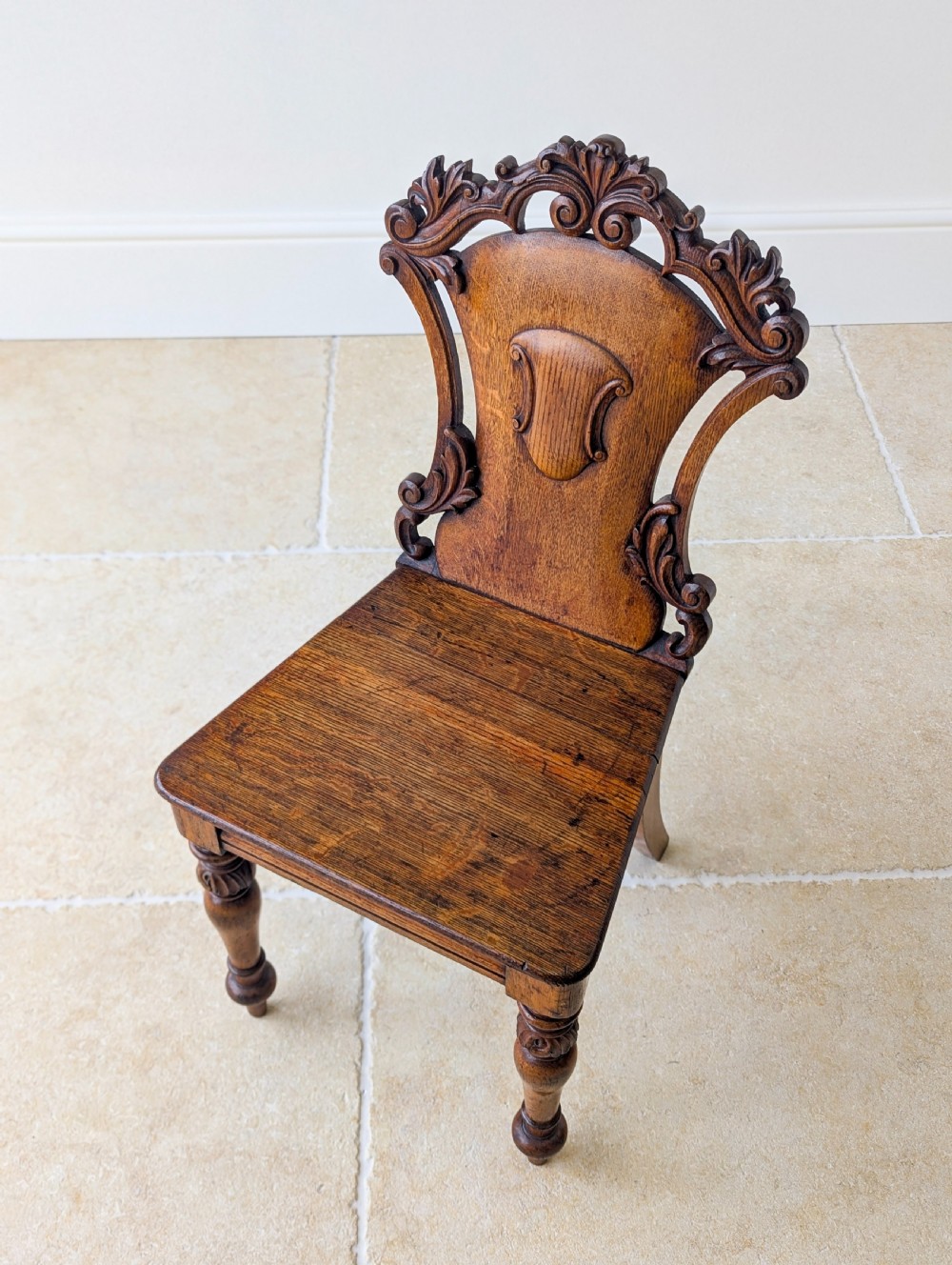 A pair of Victorian oak hall chairs featuring carved cartouche backs, flat wooden seats, and turned front legs. View XVI