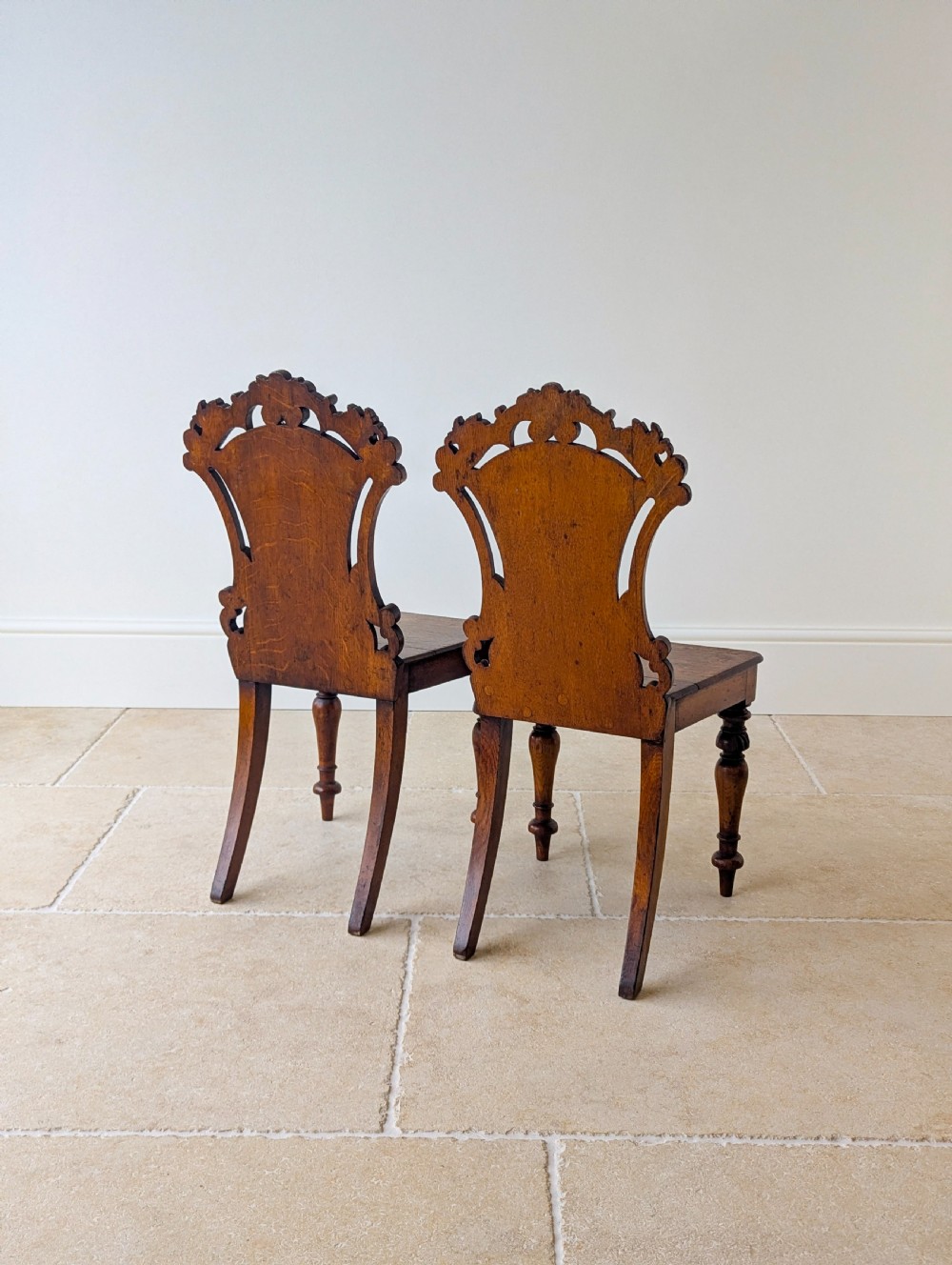 A pair of Victorian oak hall chairs featuring carved cartouche backs, flat wooden seats, and turned front legs. View XVII
