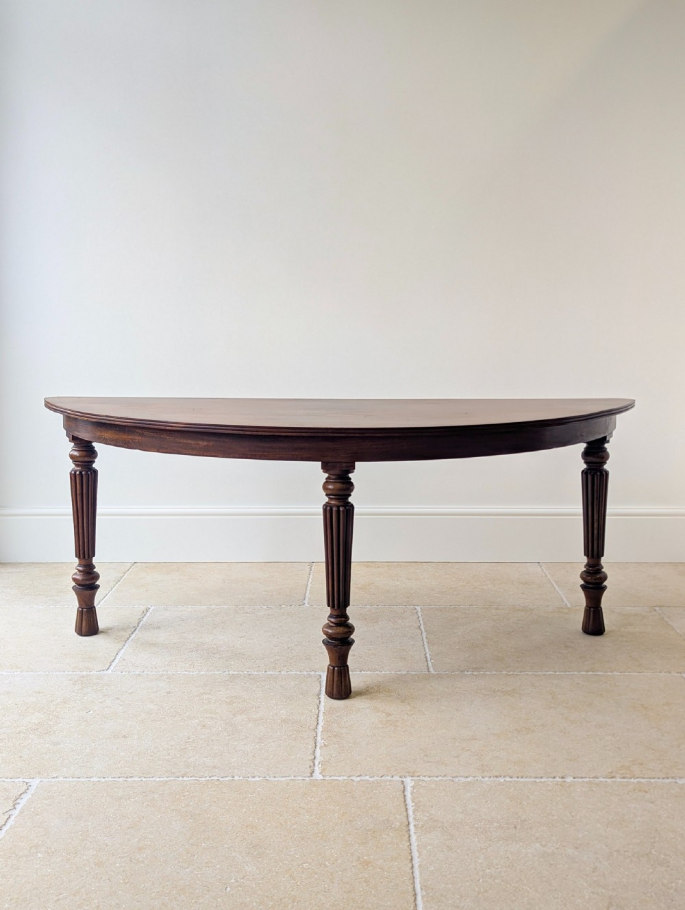 An antique Victorian demilune mahogany console table featuring a semi-circular top supported by three turned and reeded legs.