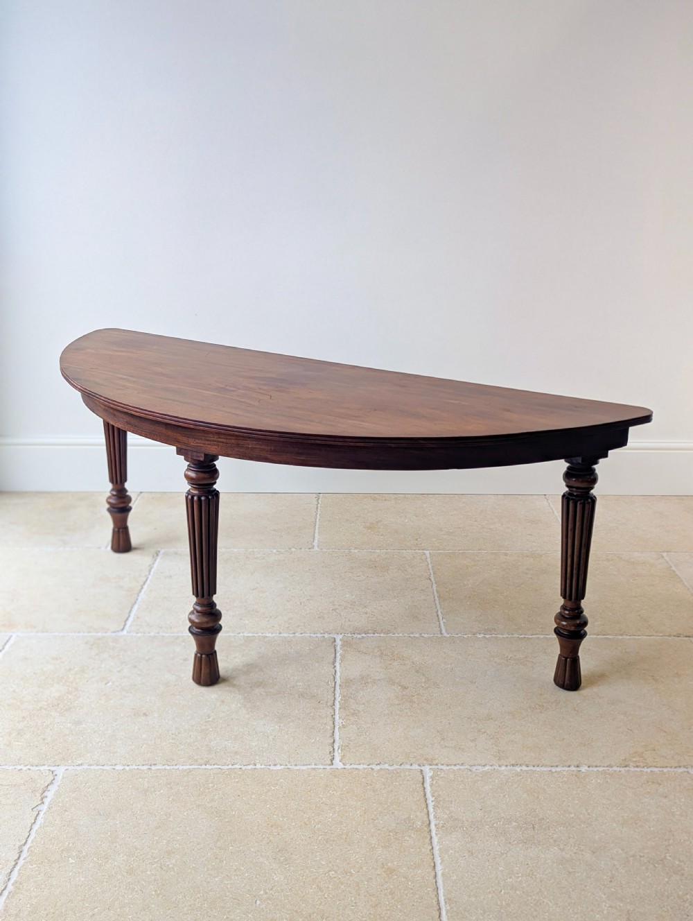 An antique Victorian demilune mahogany console table featuring a semi-circular top supported by three turned and reeded legs. View II