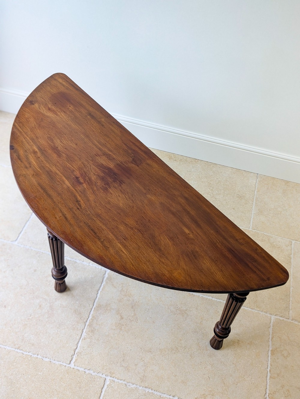 An antique Victorian demilune mahogany console table featuring a semi-circular top supported by three turned and reeded legs. View III