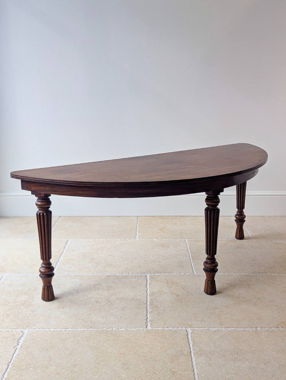 An antique Victorian demilune mahogany console table featuring a semi-circular top supported by three turned and reeded legs. View V