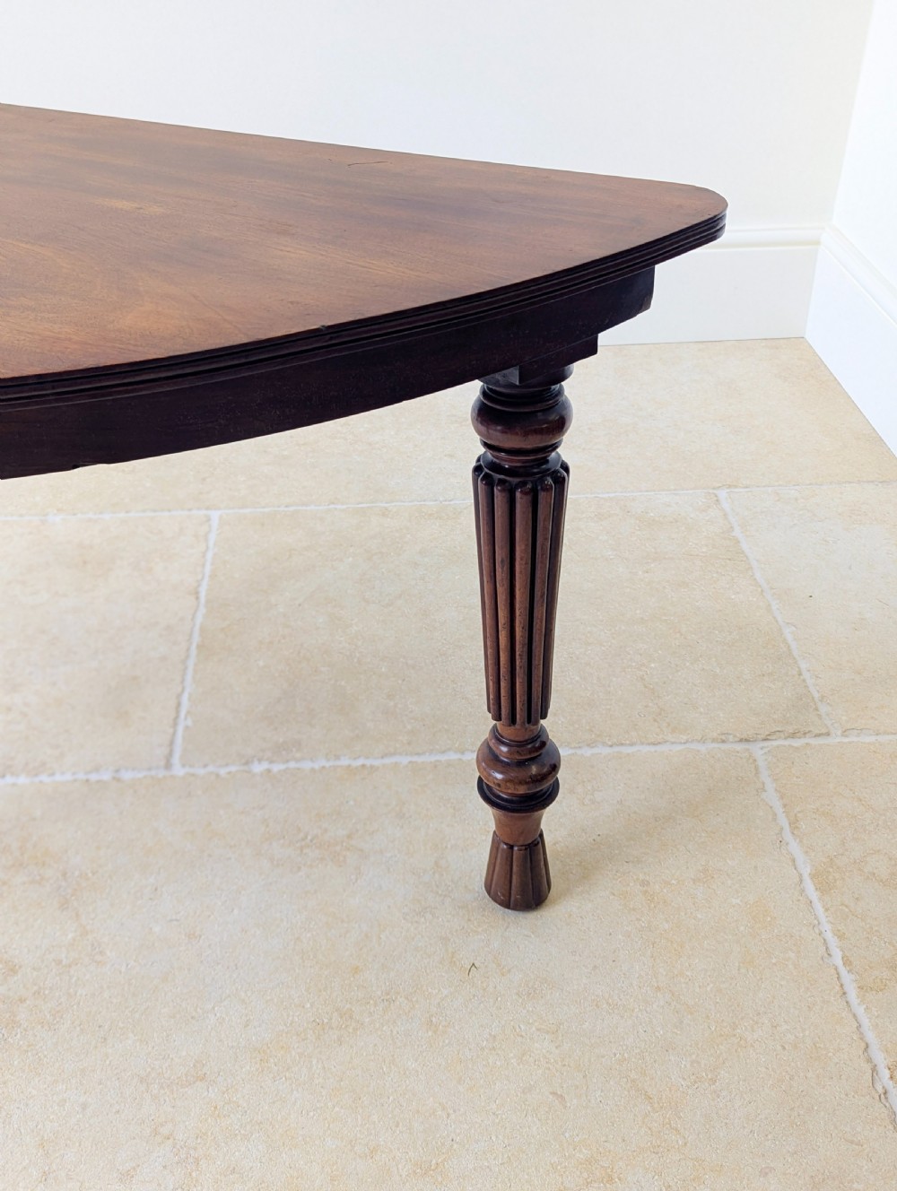 An antique Victorian demilune mahogany console table featuring a semi-circular top supported by three turned and reeded legs. View VI