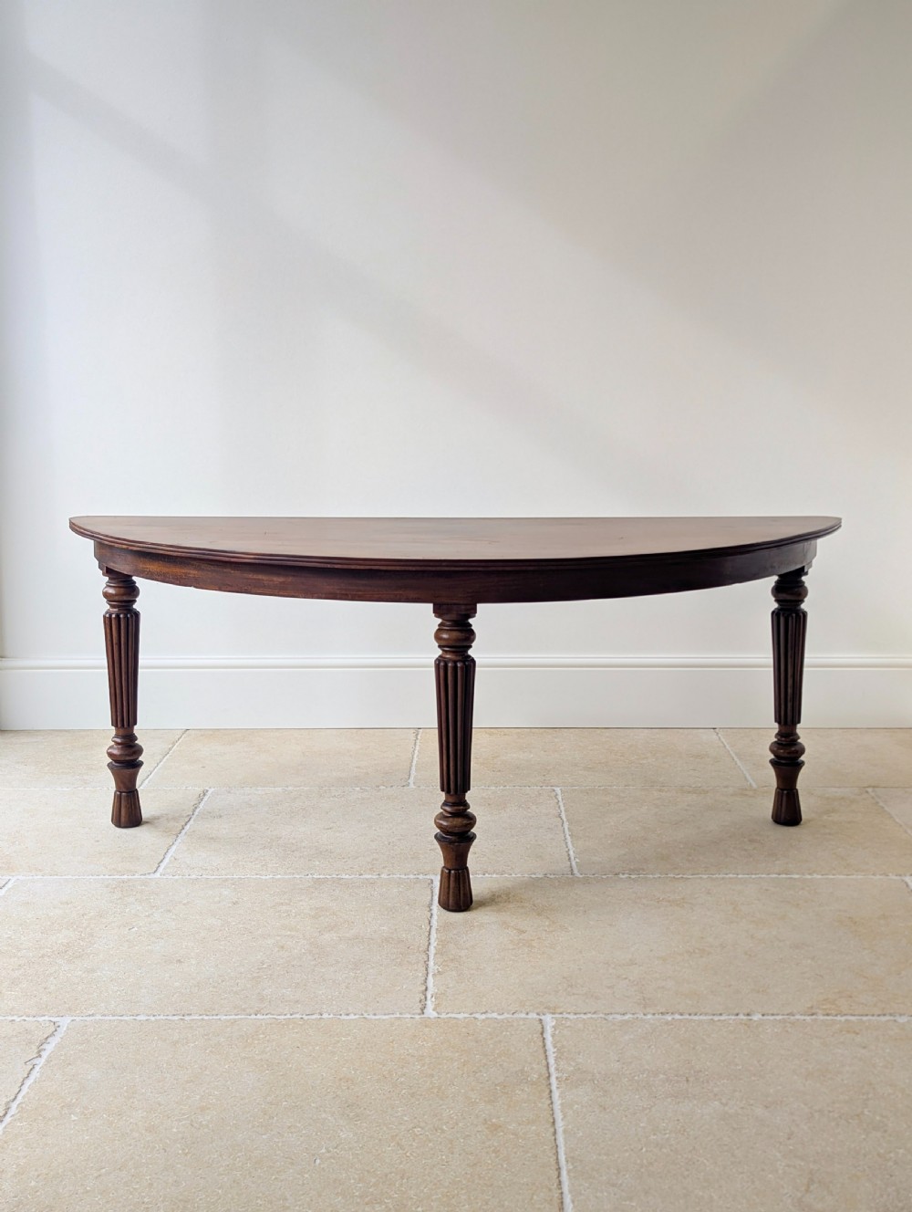An antique Victorian demilune mahogany console table featuring a semi-circular top supported by three turned and reeded legs. View VII