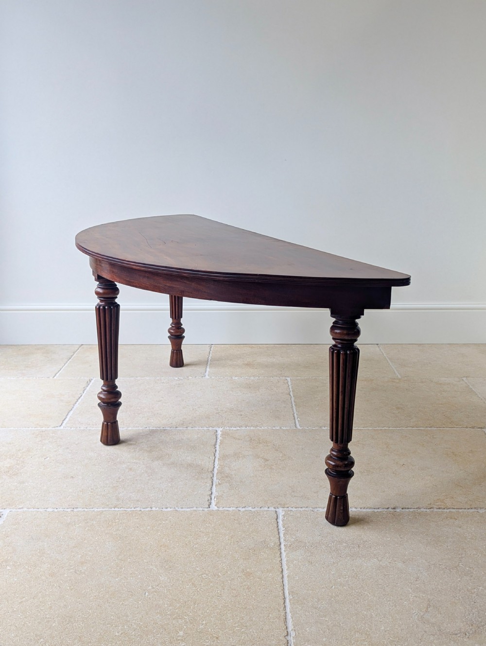 An antique Victorian demilune mahogany console table featuring a semi-circular top supported by three turned and reeded legs. View IX