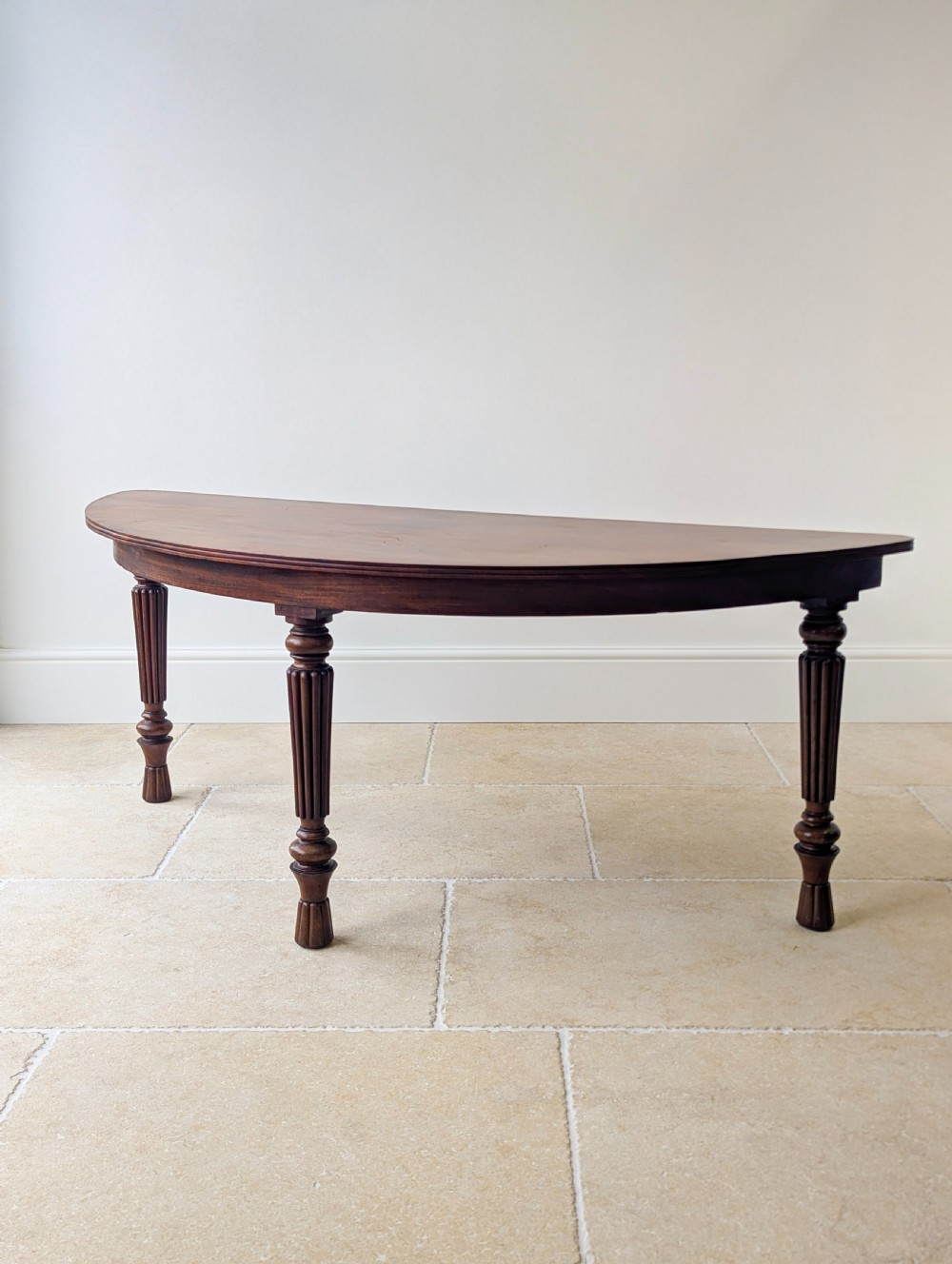 An antique Victorian demilune mahogany console table featuring a semi-circular top supported by three turned and reeded legs. View XI