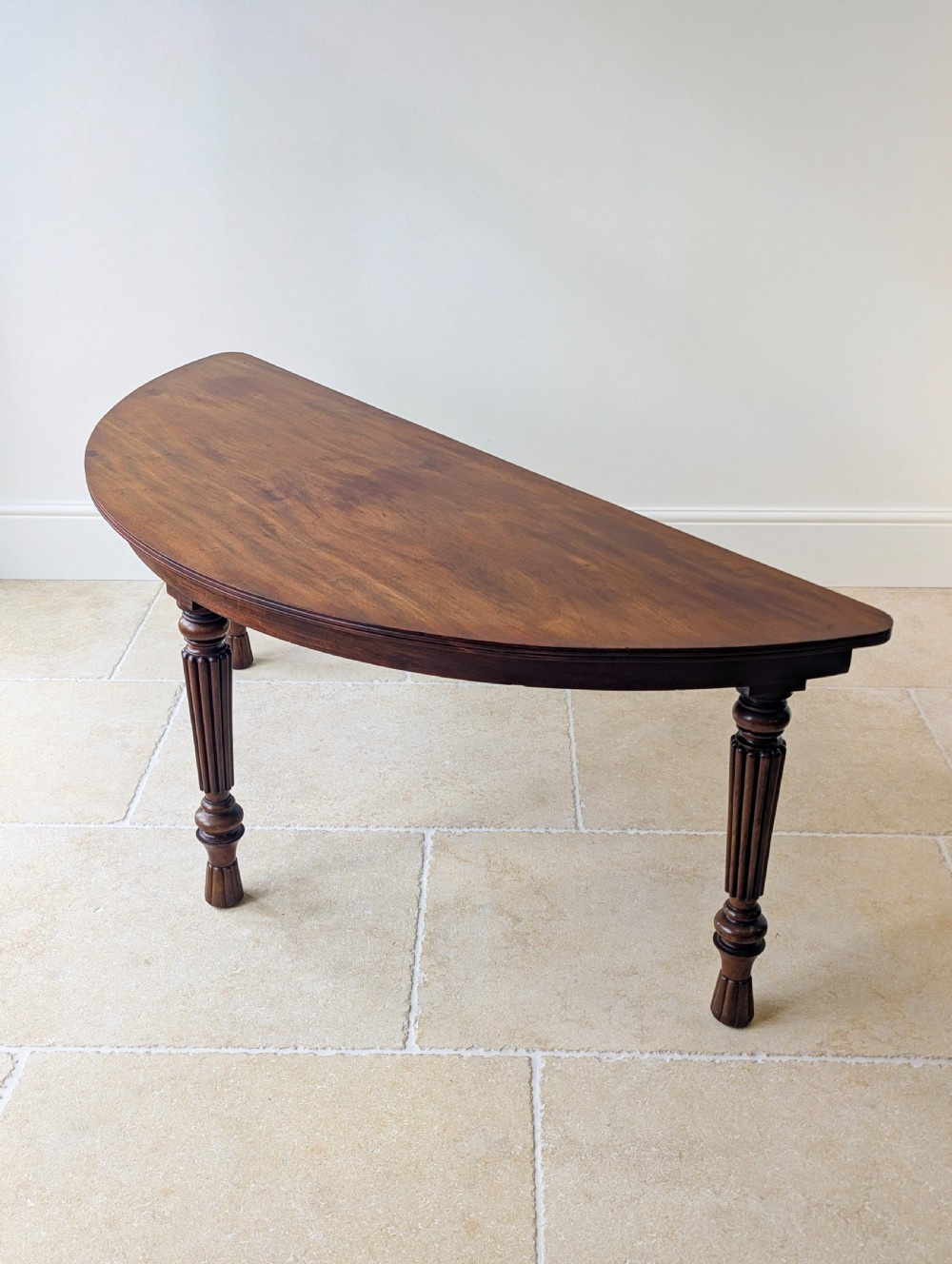 An antique Victorian demilune mahogany console table featuring a semi-circular top supported by three turned and reeded legs. View XIII