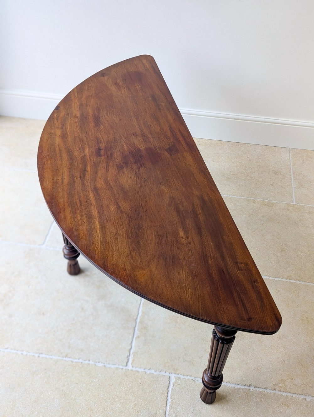 An antique Victorian demilune mahogany console table featuring a semi-circular top supported by three turned and reeded legs. View XIV