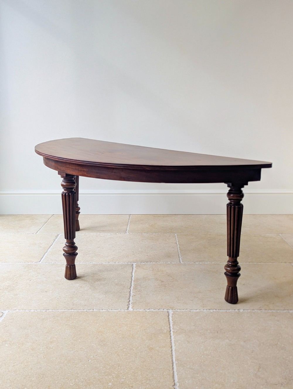 An antique Victorian demilune mahogany console table featuring a semi-circular top supported by three turned and reeded legs. View XV