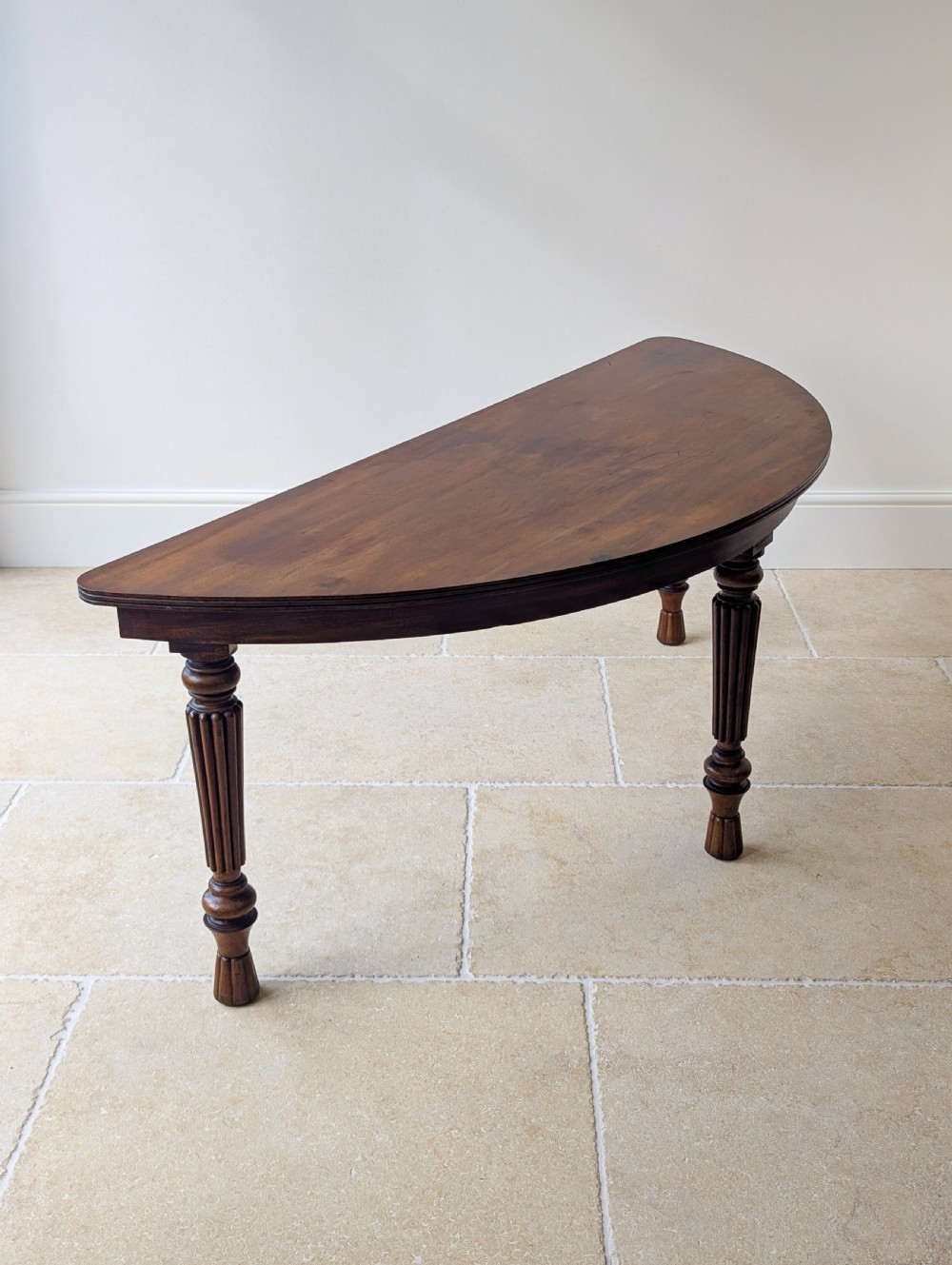 An antique Victorian demilune mahogany console table featuring a semi-circular top supported by three turned and reeded legs. View XVI