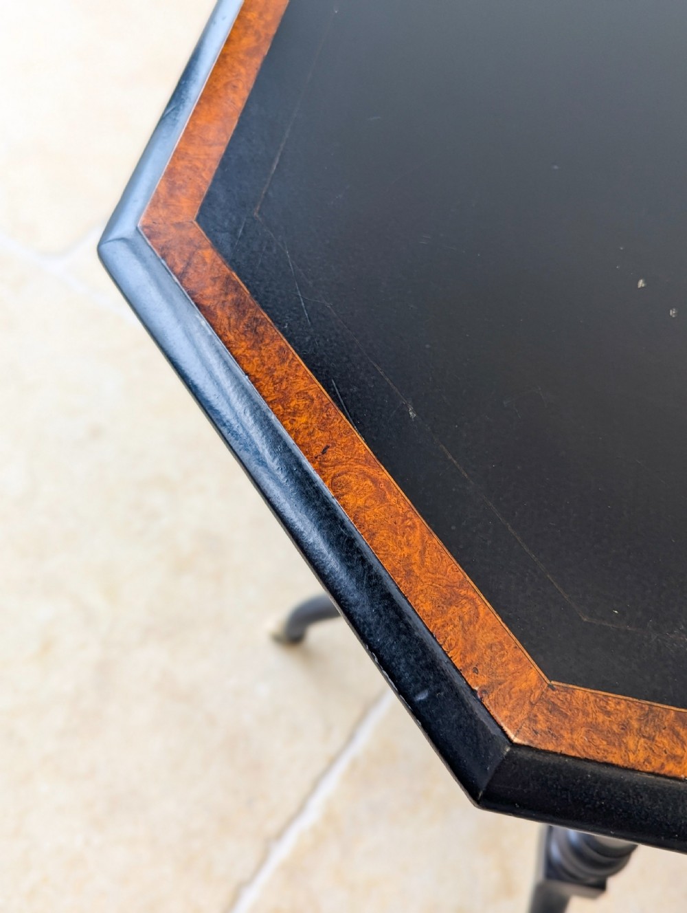 A late Victorian ebonised octagonal occasional table featuring turned legs, gilt highlights, cross stretchers, and brass castors. View II