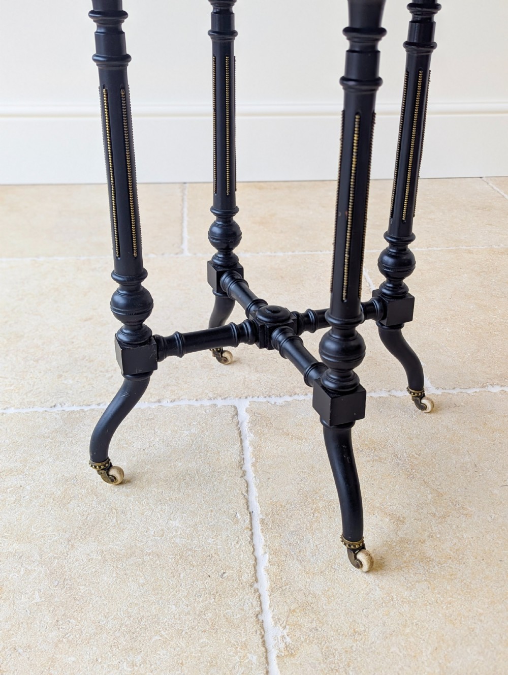 A late Victorian ebonised octagonal occasional table featuring turned legs, gilt highlights, cross stretchers, and brass castors. View IV