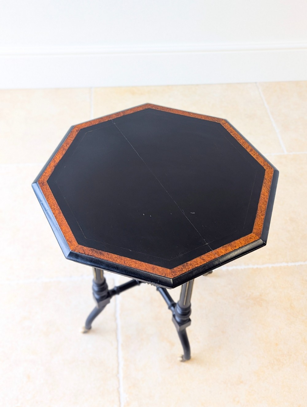 A late Victorian ebonised octagonal occasional table featuring turned legs, gilt highlights, cross stretchers, and brass castors. View VI