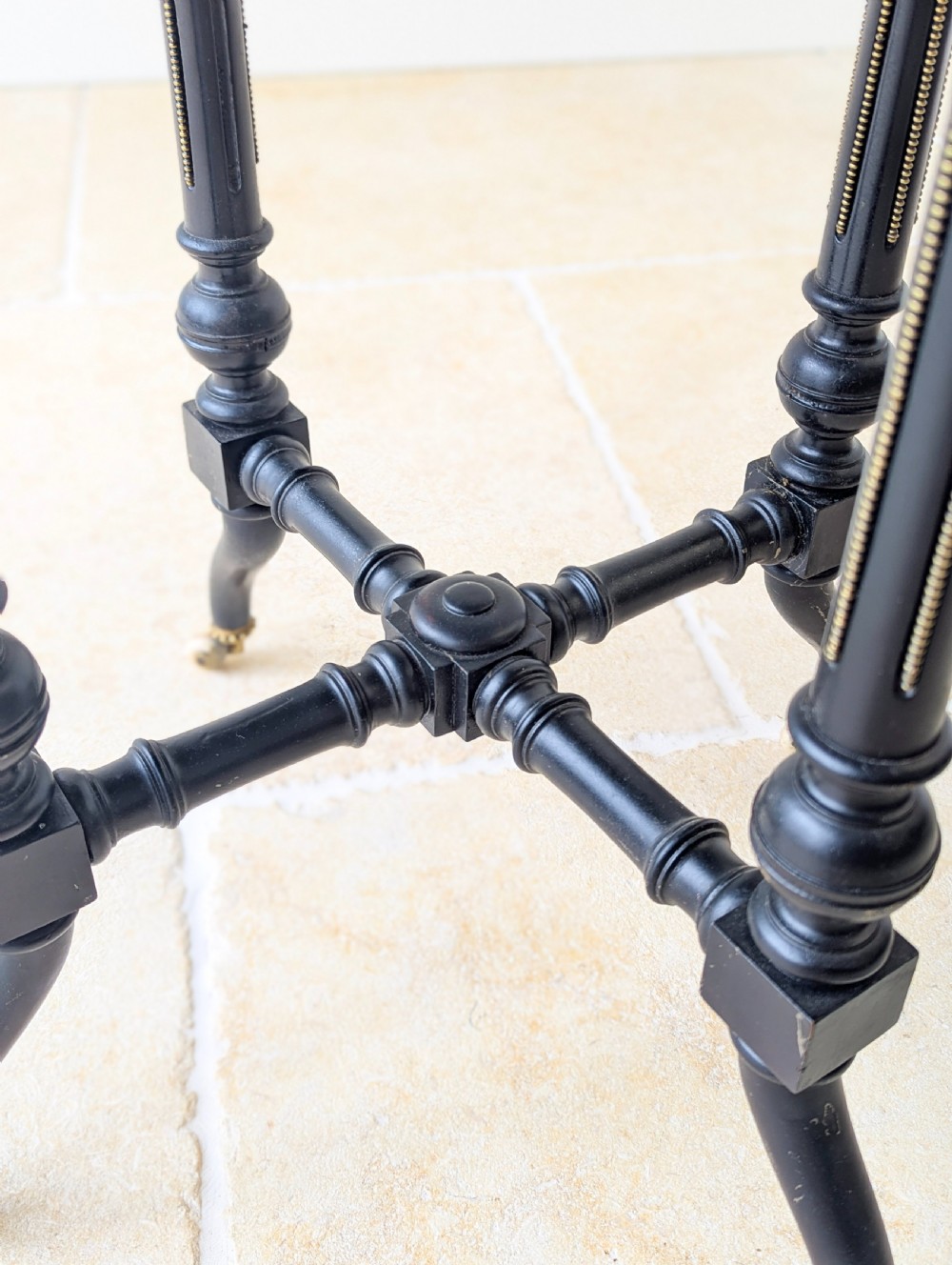 A late Victorian ebonised octagonal occasional table featuring turned legs, gilt highlights, cross stretchers, and brass castors. View X