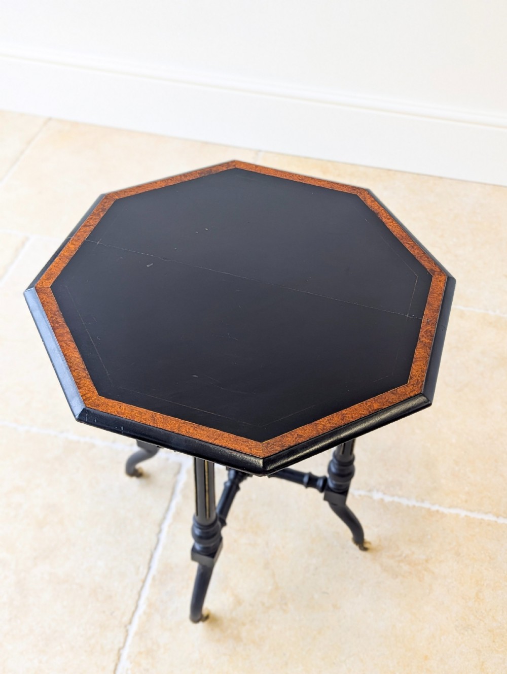 A late Victorian ebonised octagonal occasional table featuring turned legs, gilt highlights, cross stretchers, and brass castors. View XII