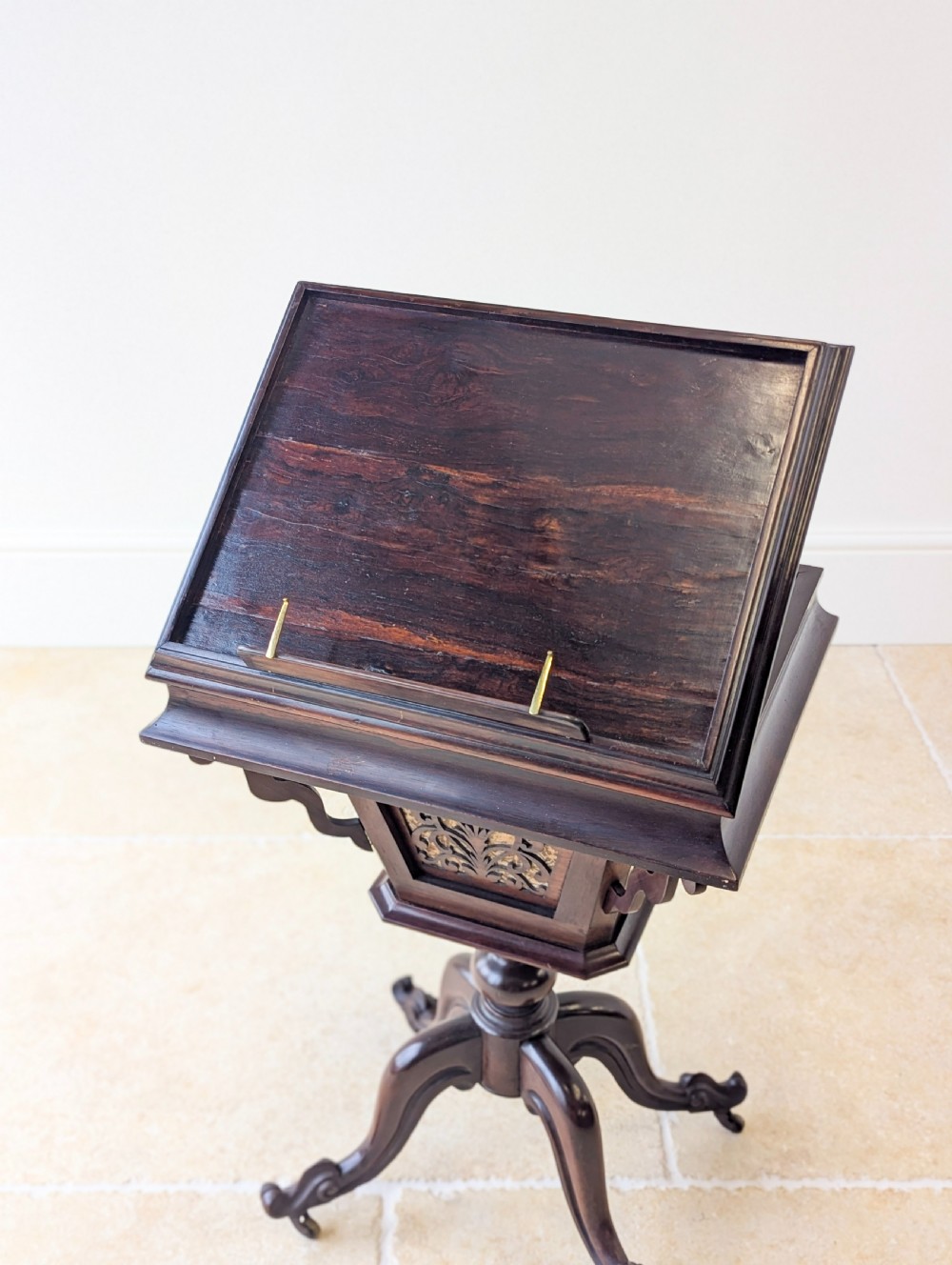 A dark brown rosewood Victorian sewing and reading table featuring an adjustable slanted lid with brass page holders, carved fretwork sides, a turned pedestal column, and four scrolled feet. View X