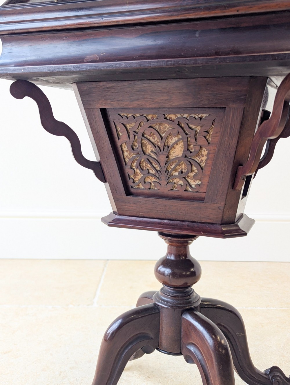 A dark brown rosewood Victorian sewing and reading table featuring an adjustable slanted lid with brass page holders, carved fretwork sides, a turned pedestal column, and four scrolled feet. View XVI