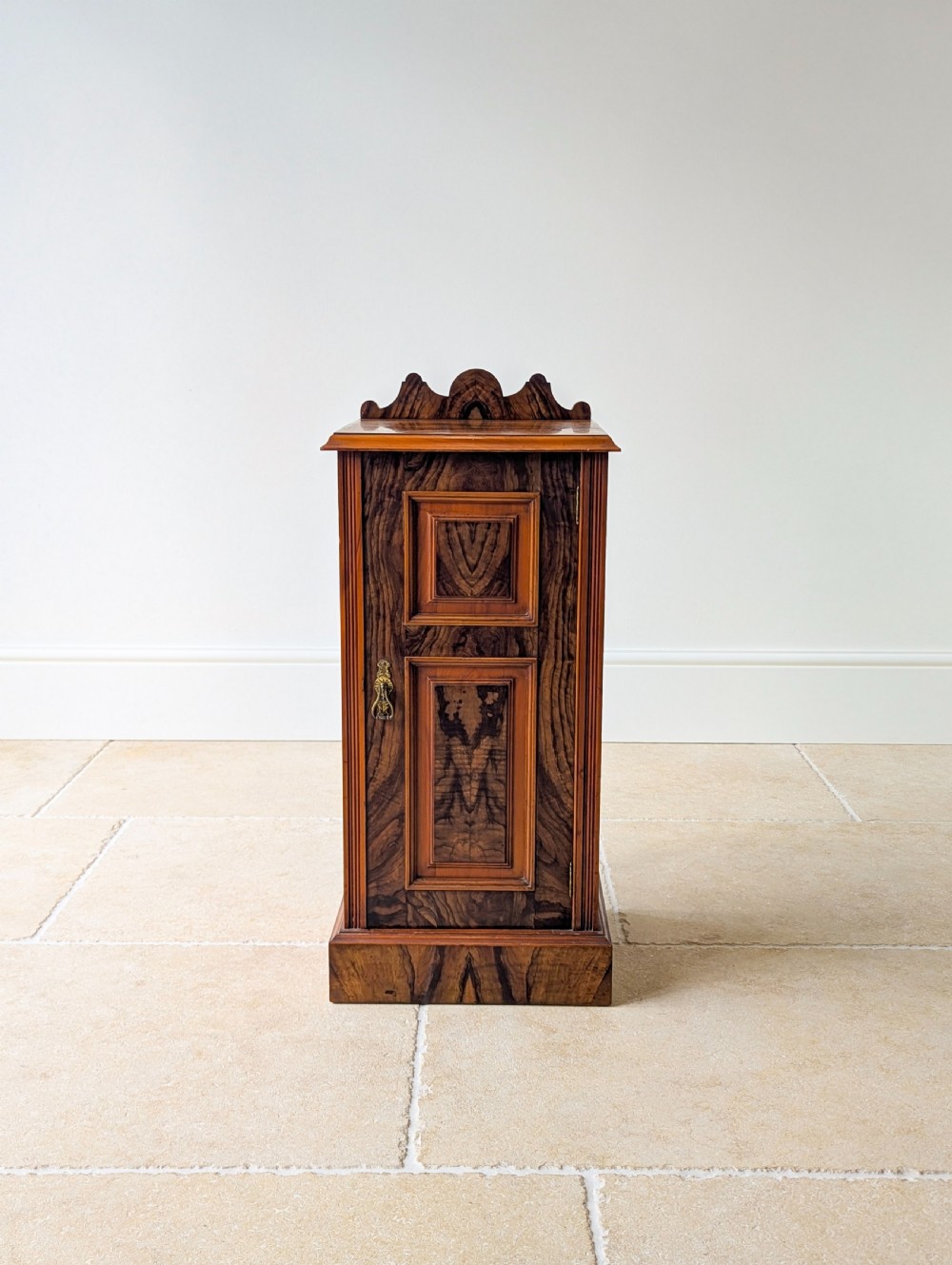 A late Victorian mahogany and exotic wood bedside cupboard featuring a carved top gallery, panelled door with brass drop handle, and a solid plinth base. View III