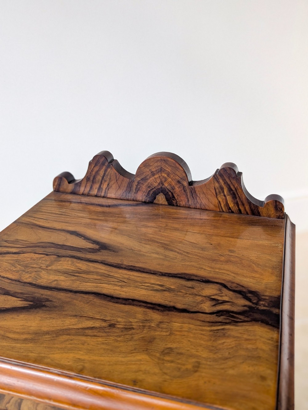 A late Victorian mahogany and exotic wood bedside cupboard featuring a carved top gallery, panelled door with brass drop handle, and a solid plinth base. View VI